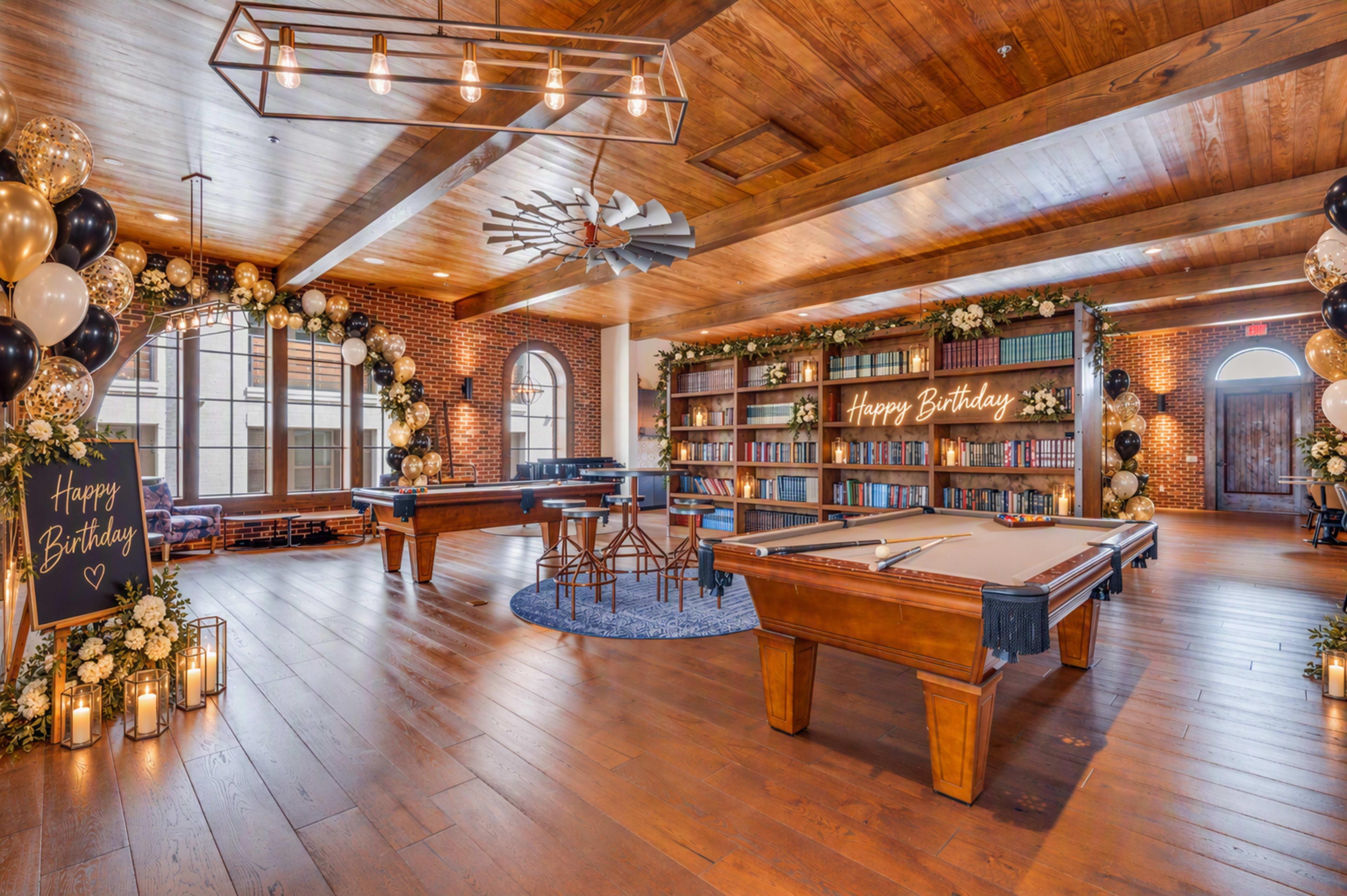 The image shows a spacious indoor party venue decorated with balloons, flowers, and a "Happy Birthday" sign, featuring a pool table and bookshelves.