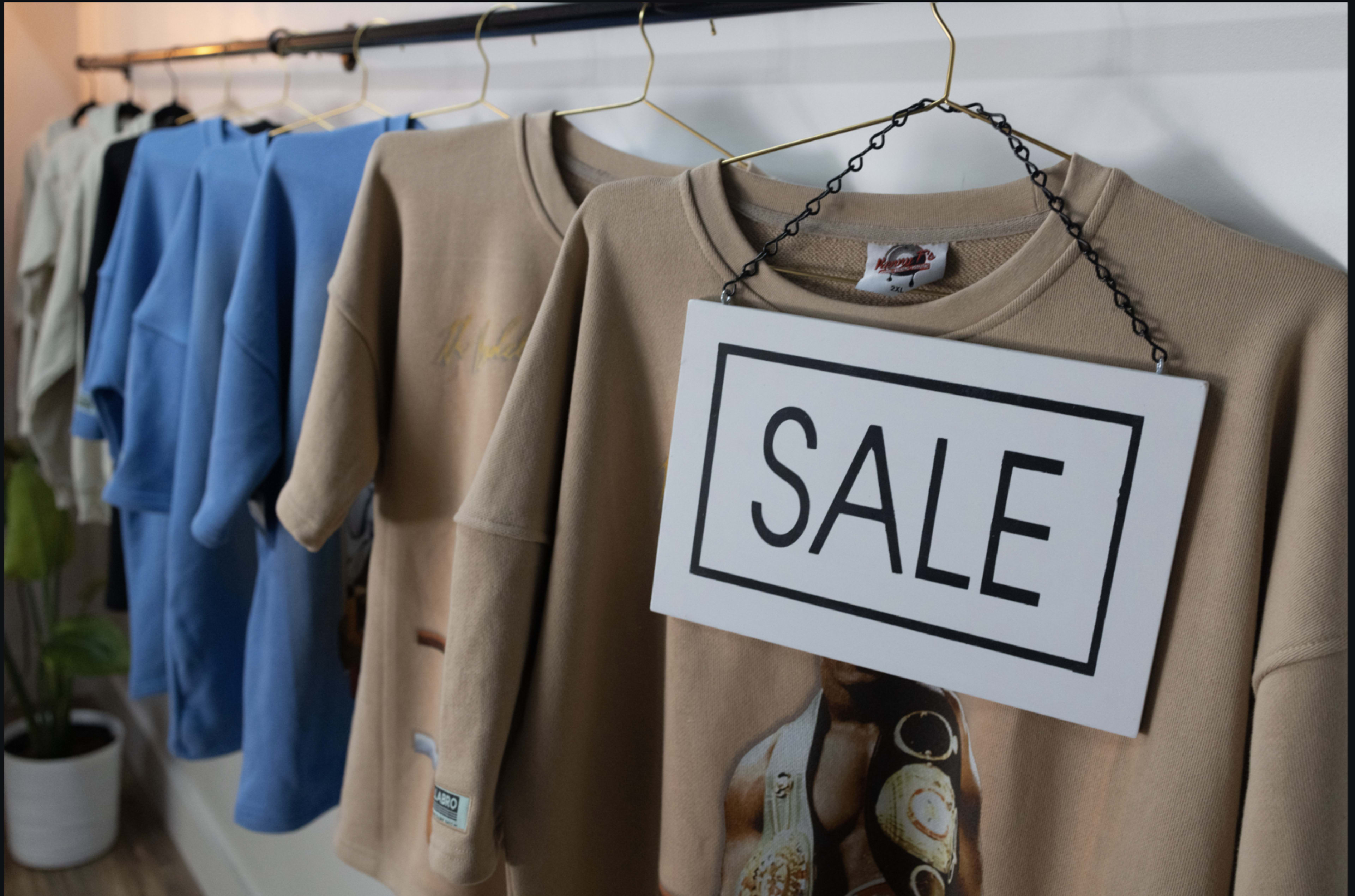 A row of colorful t-shirts is displayed on hangers, with a "SALE" sign hanging prominently in front.