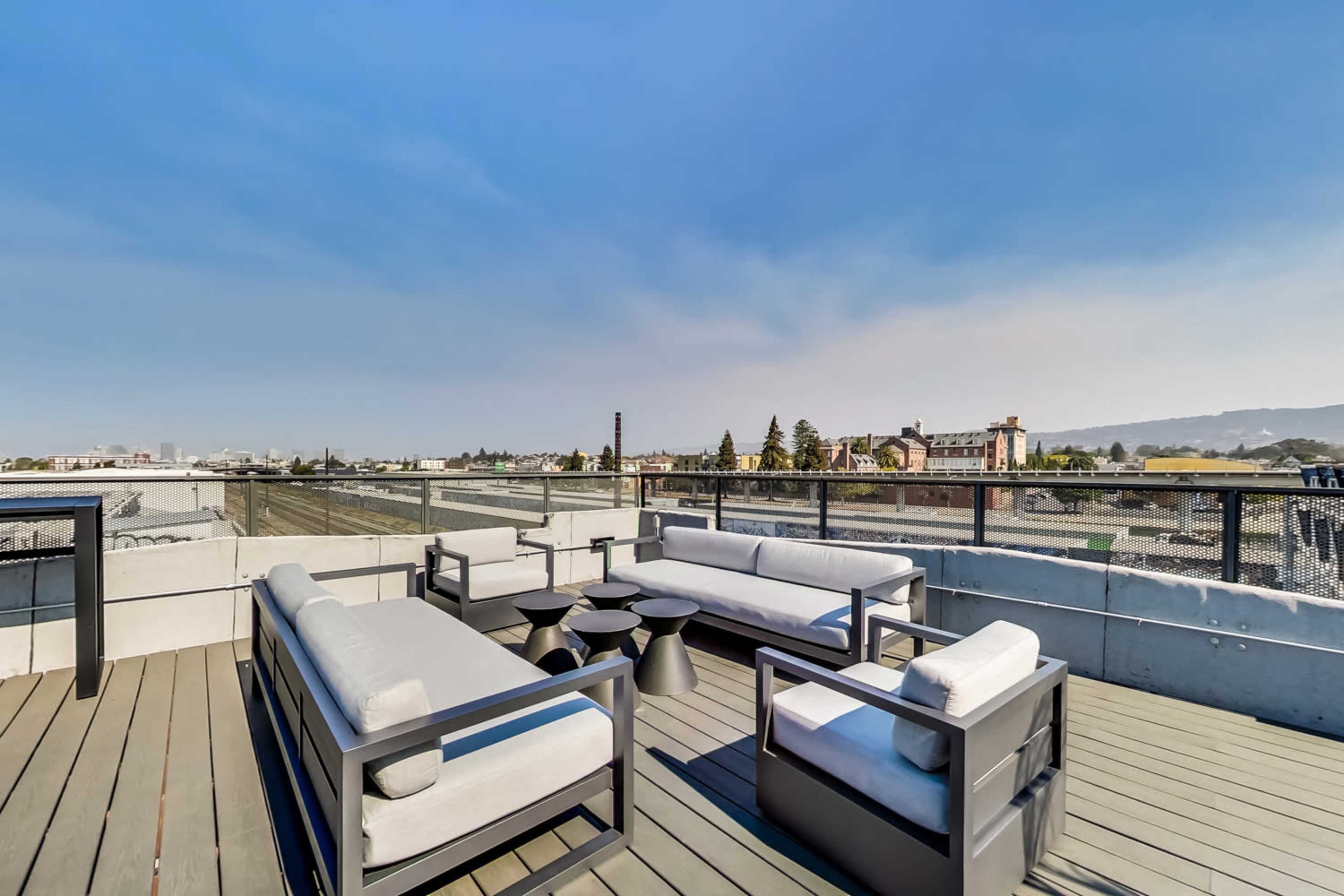 A rooftop deck with modern seating, a circular table, and a view of surrounding buildings and landscape.