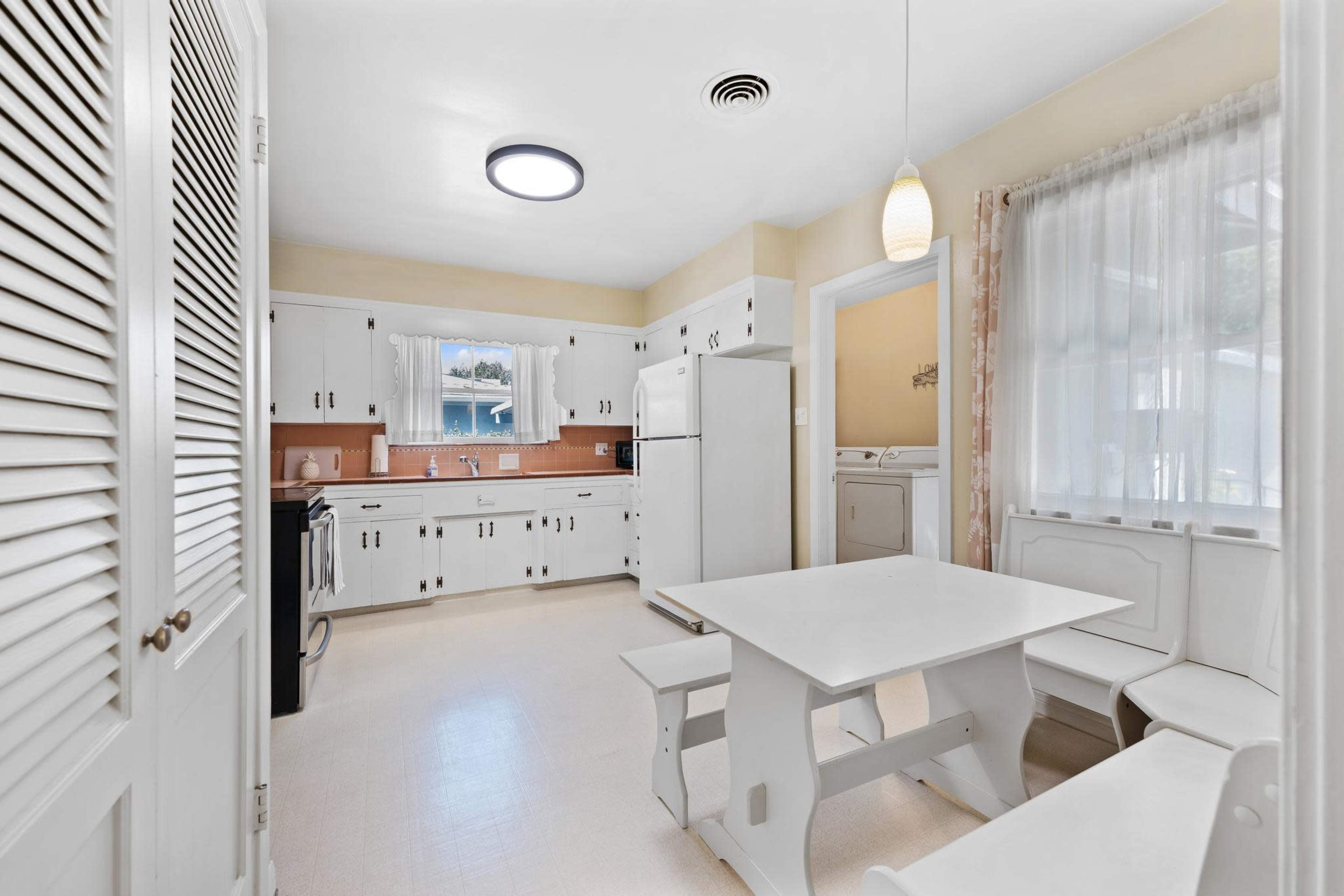 A bright kitchen with white cabinetry, a central table, and a window above the sink.