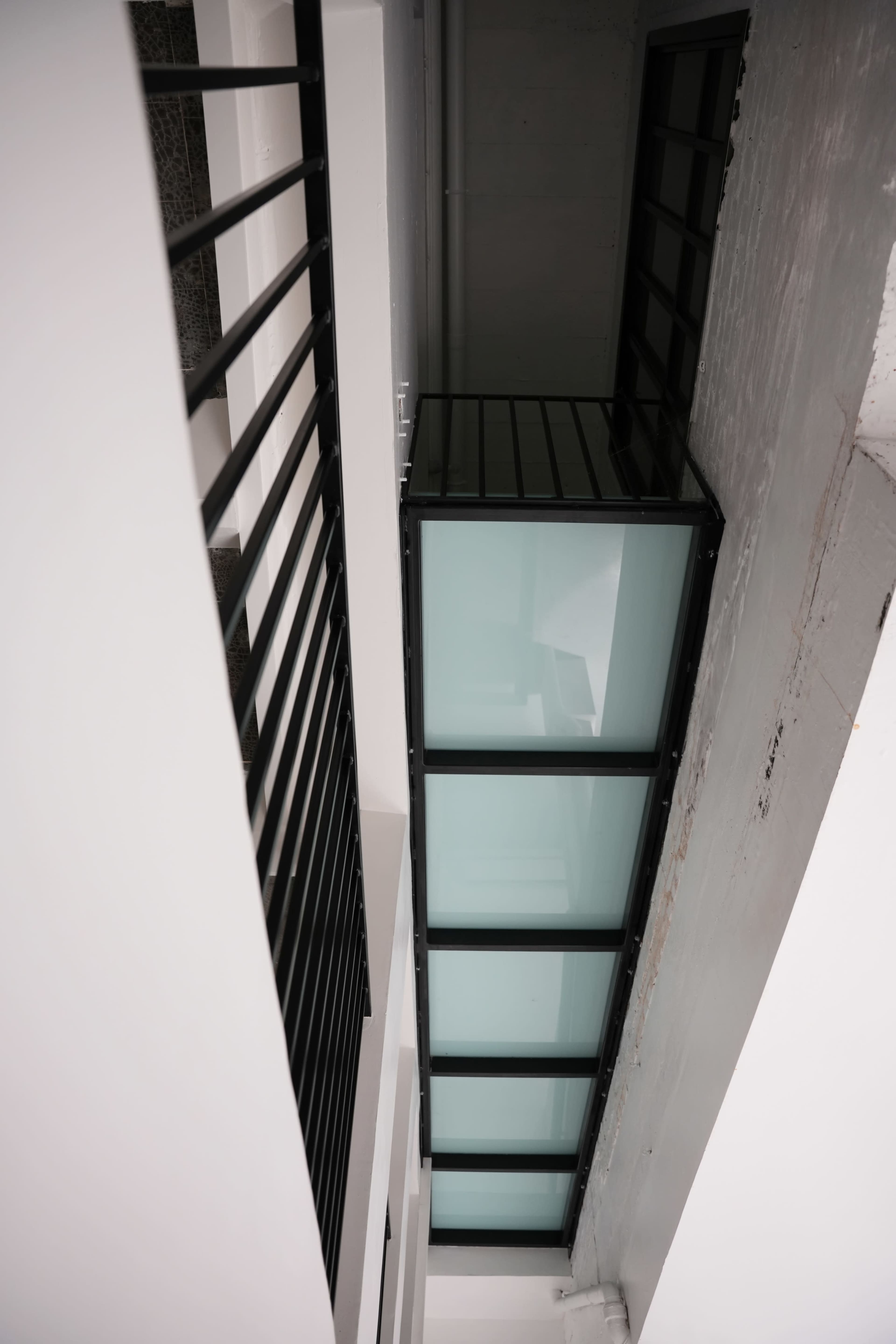 A modern building's interior featuring a glass corridor suspended between two walls, with black railings on either side.