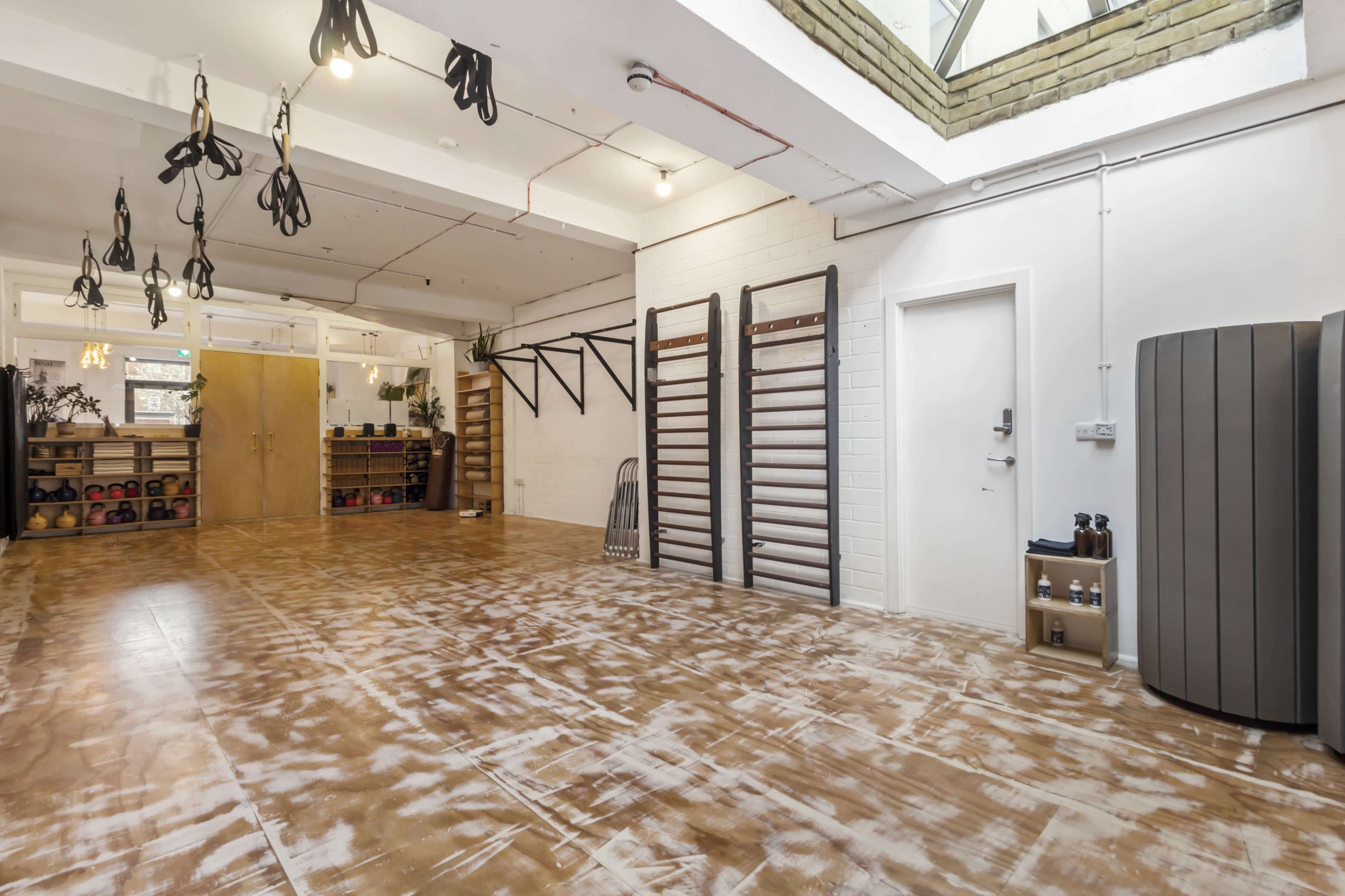 The image shows a spacious gym with workout equipment, including wall-mounted bars, kettlebells, and a large window allowing natural light to fill the area.