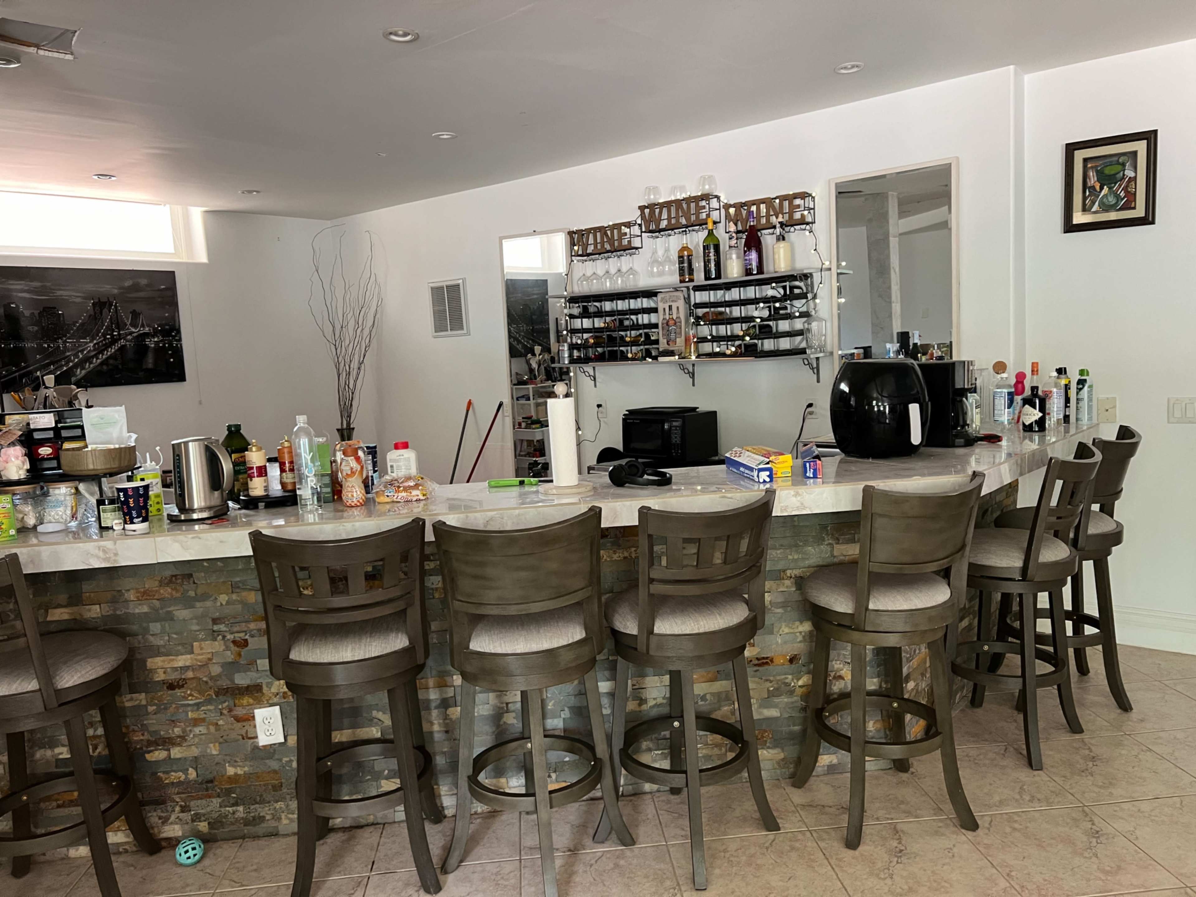 A modern kitchen bar area with eight stools, a counter decorated with various bottles and kitchen appliances, and a mirrored wall behind it.