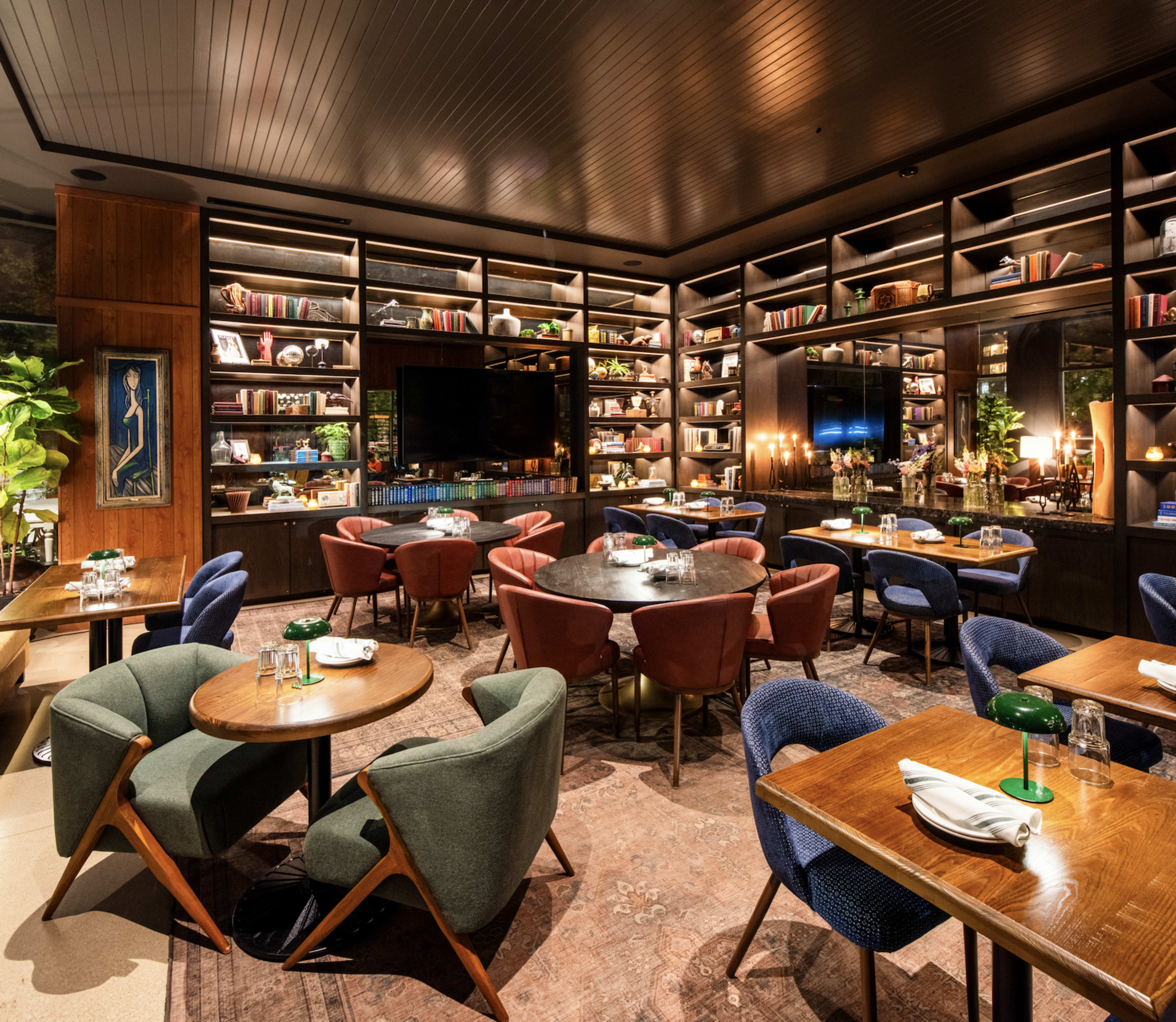 The image shows a modern restaurant with multiple dining tables surrounded by wooden shelving filled with books and decorative items.