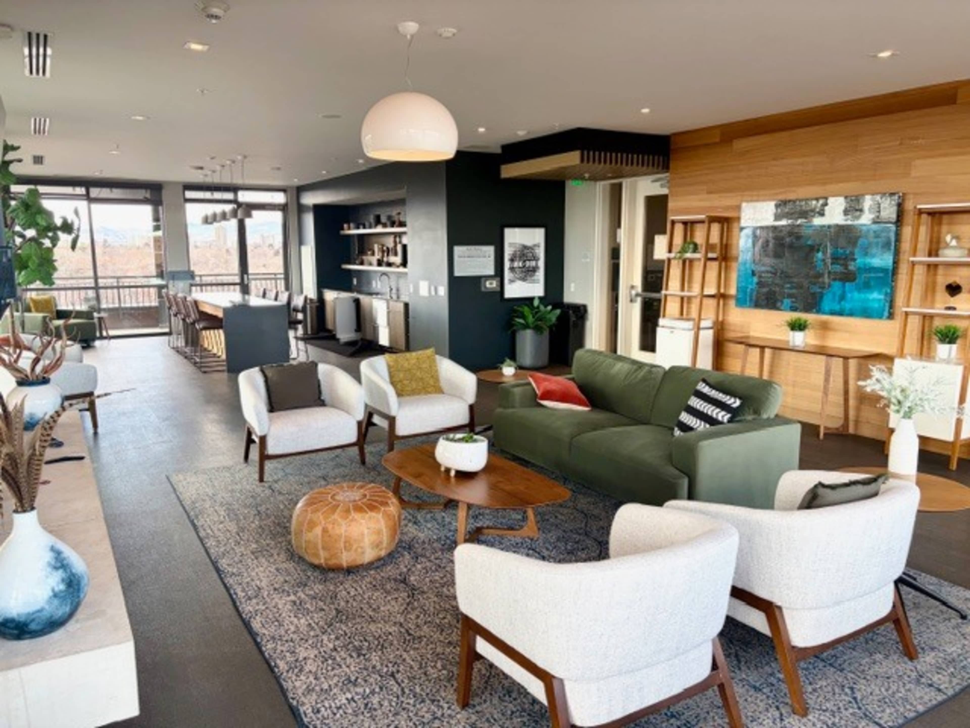The image shows a modern, stylish living room area with a green sofa, white armchairs, a wooden coffee table, and large windows providing natural light.