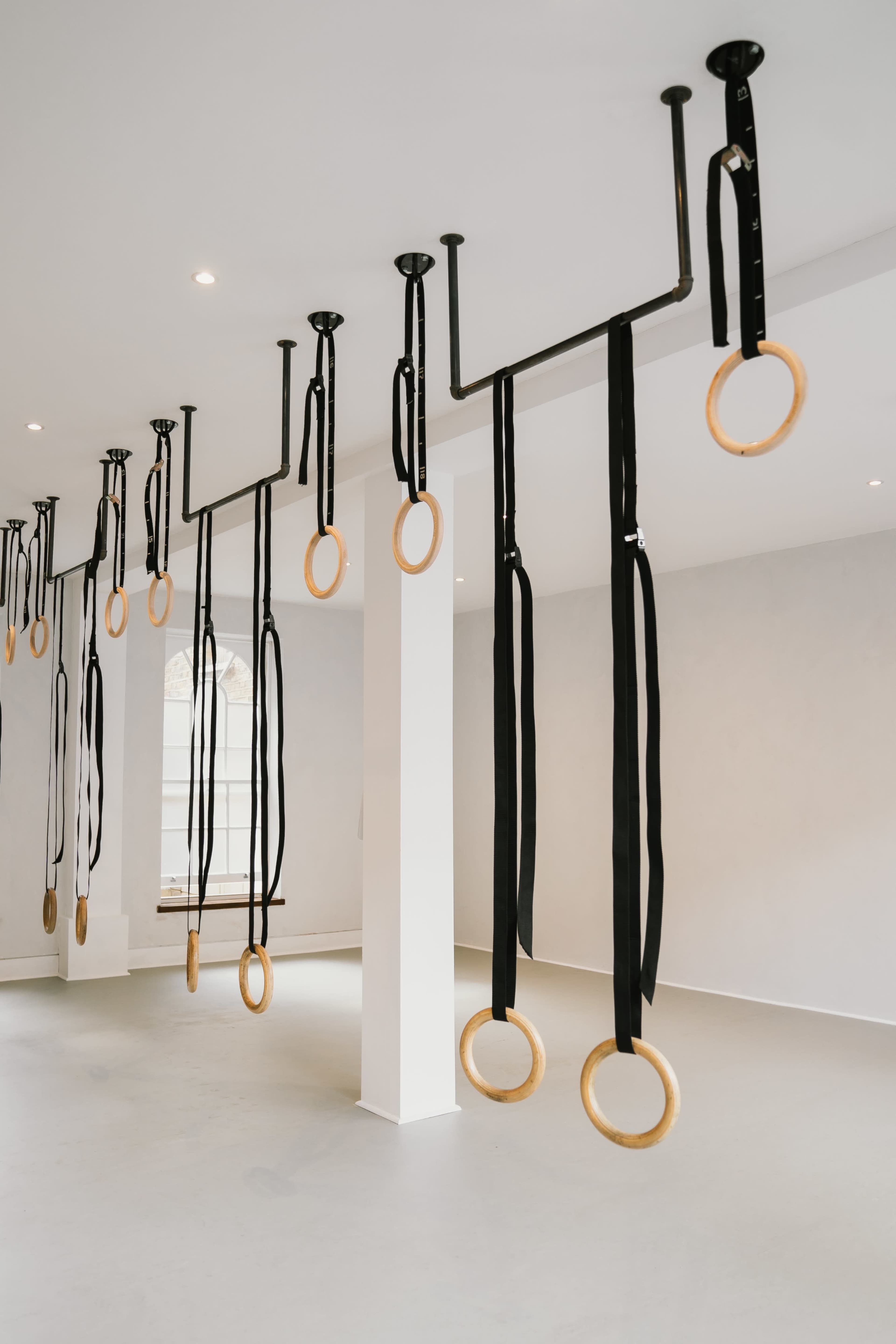 A gym interior with multiple gymnastic rings hanging from the ceiling by black straps.