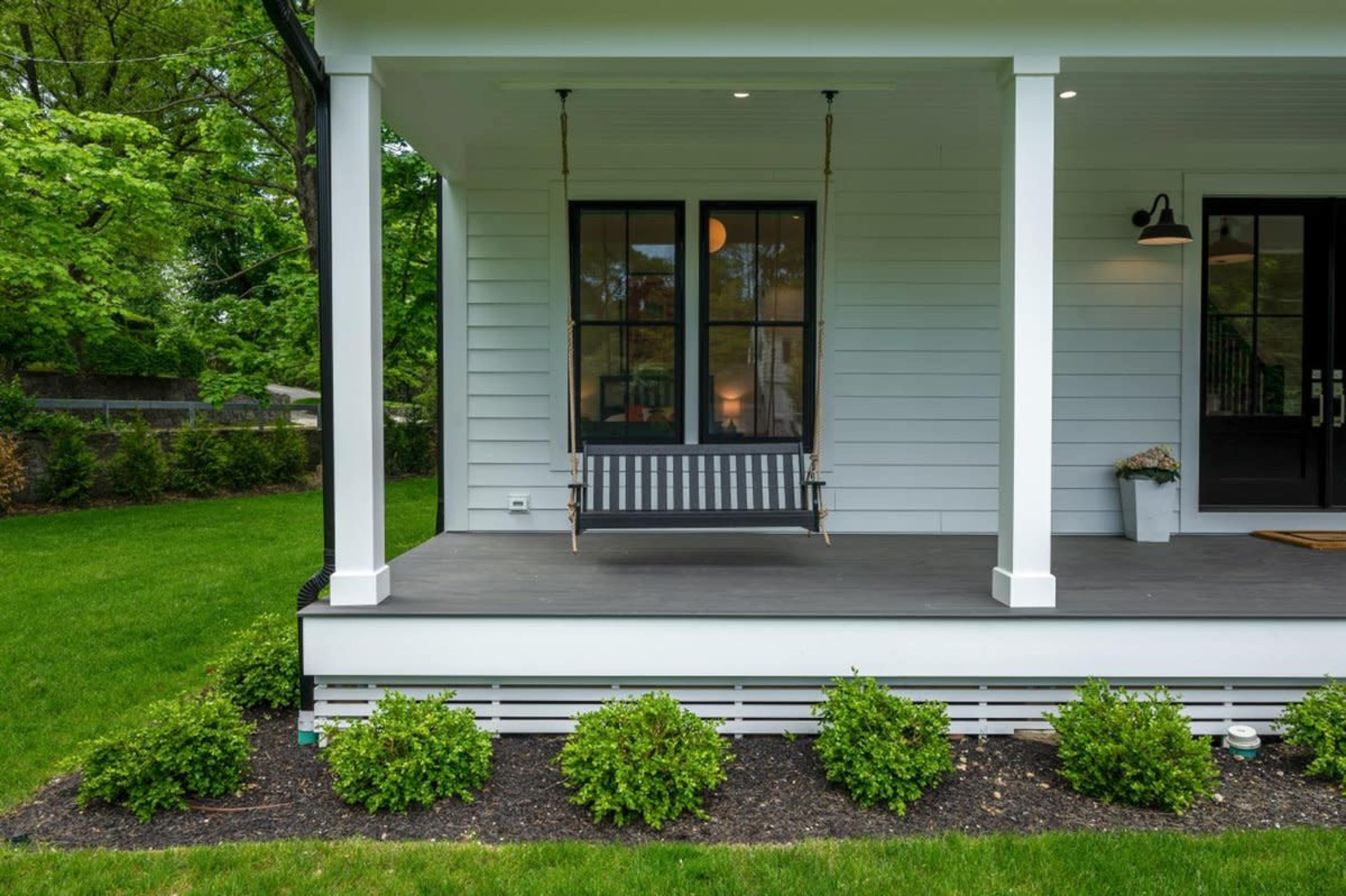 A porch featuring a swing and surrounded by a neatly trimmed lawn and shrubs.