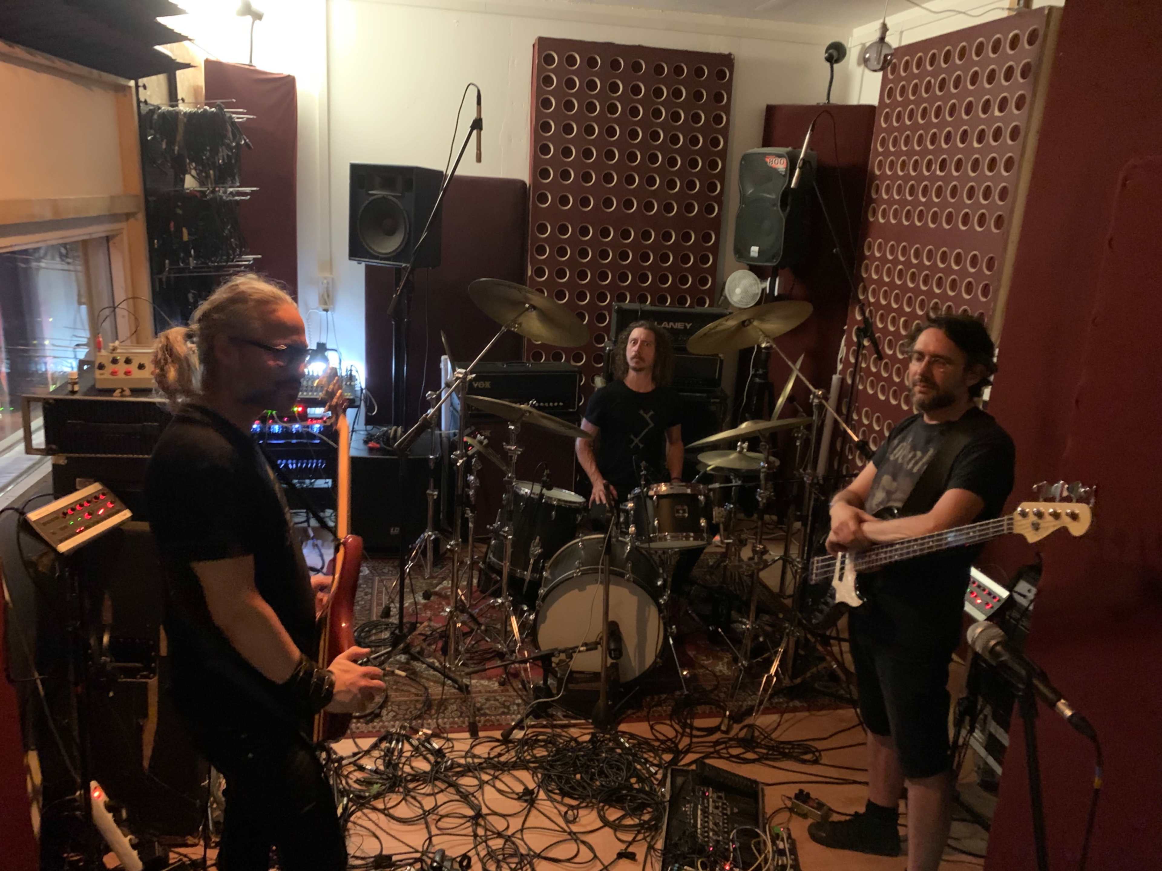 Three musicians are practicing in a soundproof room equipped with musical instruments and amplifiers.