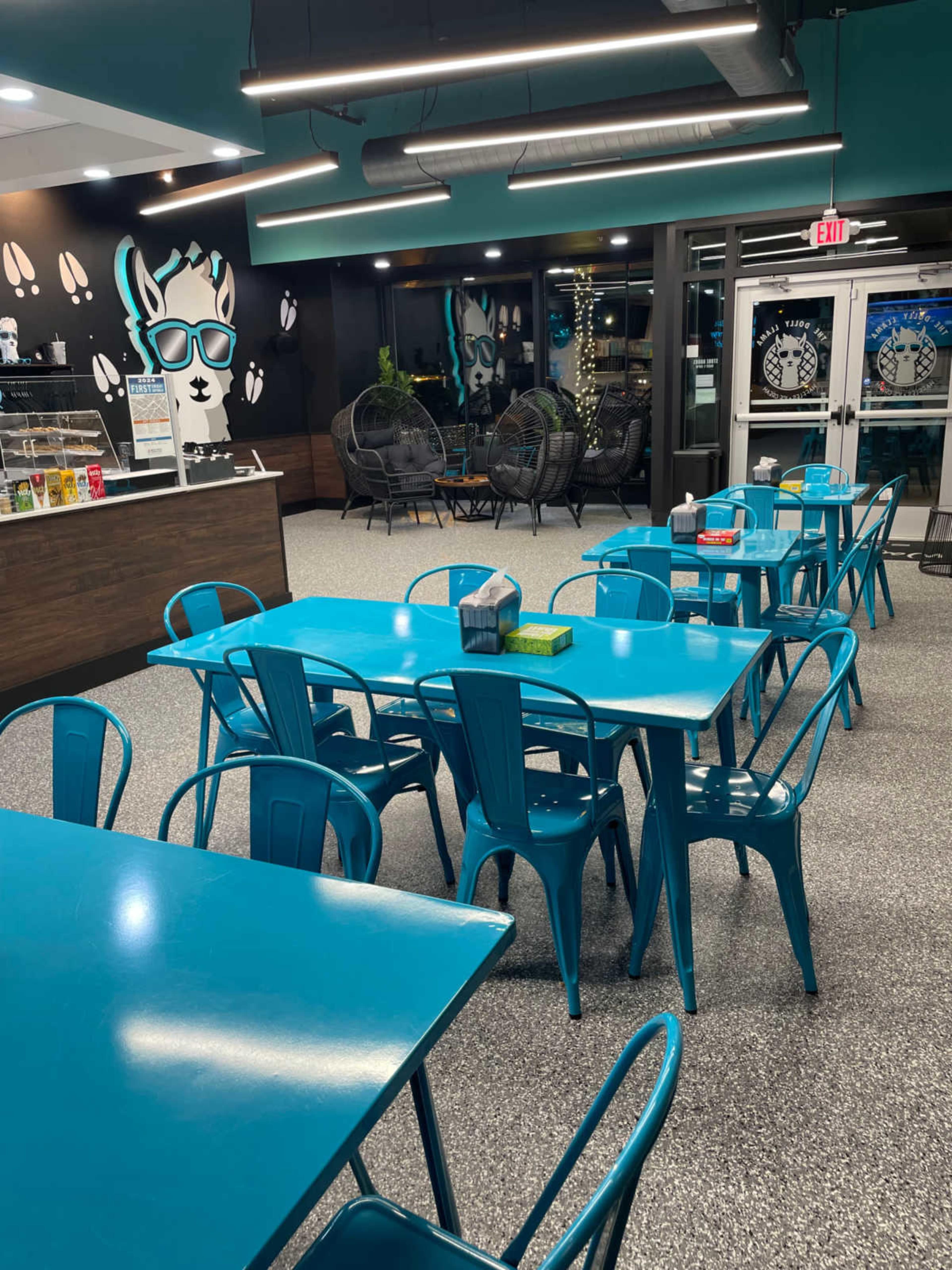 The image shows a brightly colored cafe interior with turquoise tables and chairs arranged around the space, featuring modern decor and wall art.