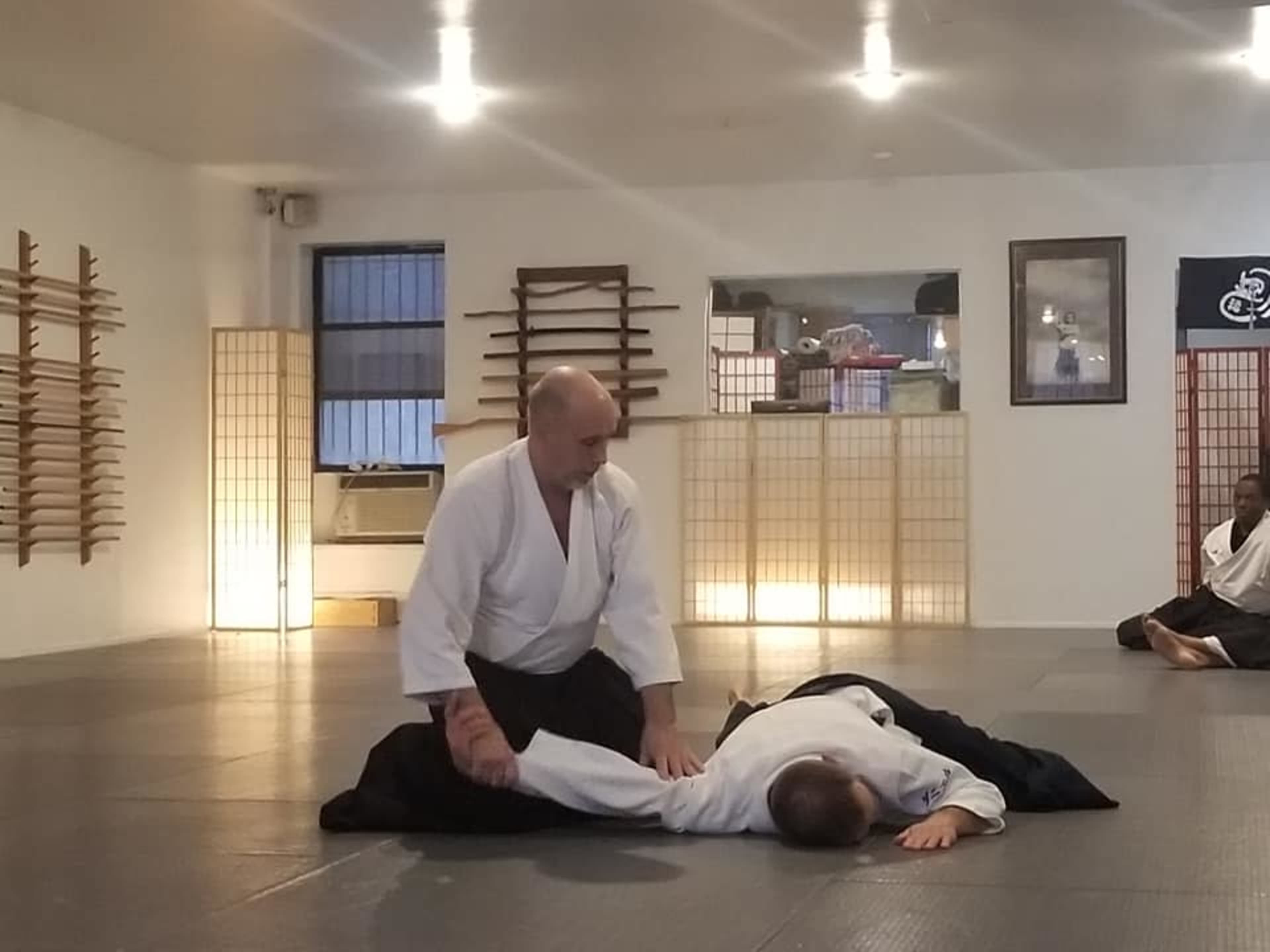 Two practitioners are engaged in a martial arts demonstration on a tatami mat in a dojo.
