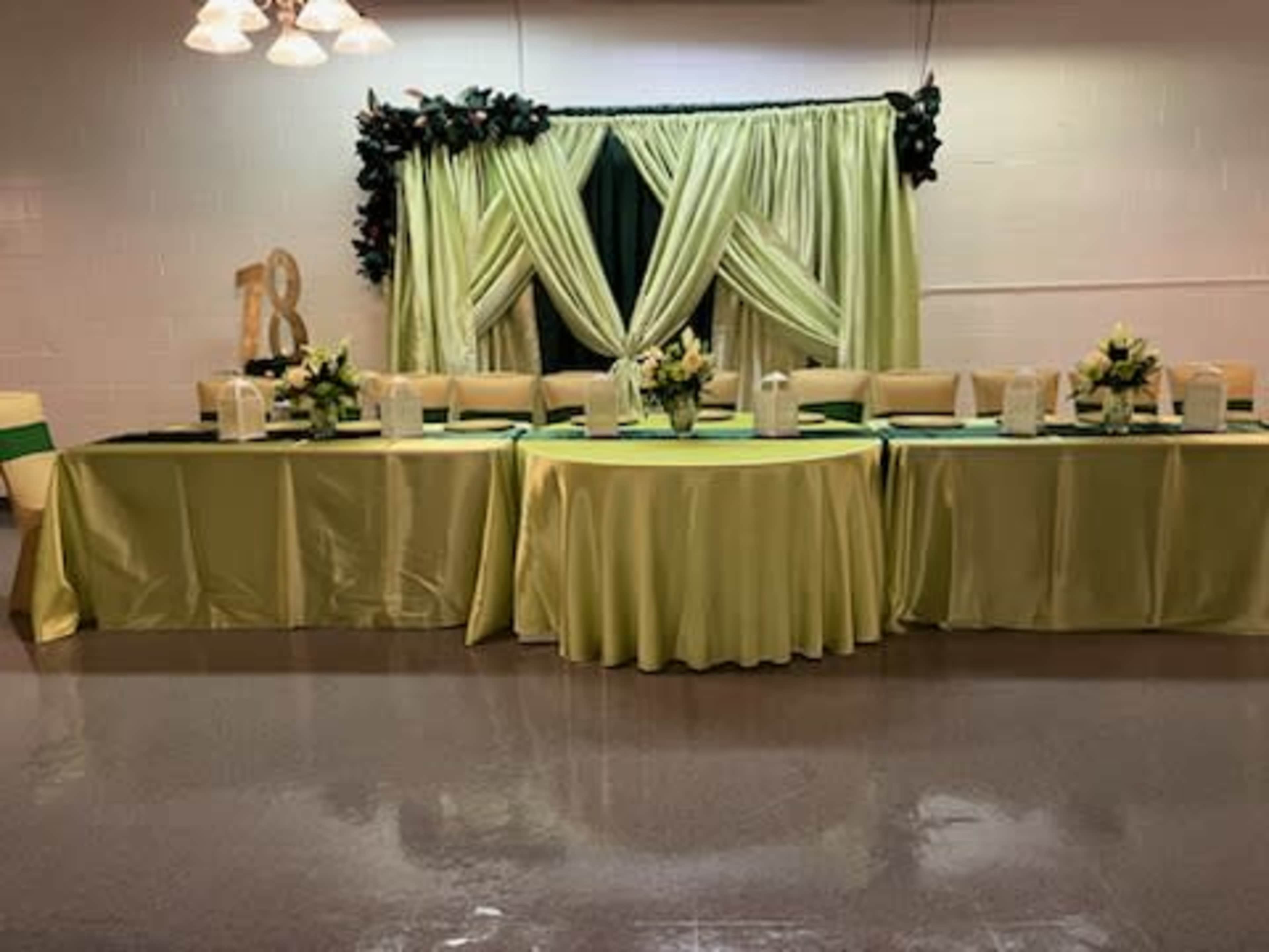 A banquet table decorated with yellow and green cloths is set up against a backdrop of draped fabric and floral arrangements for a celebration.