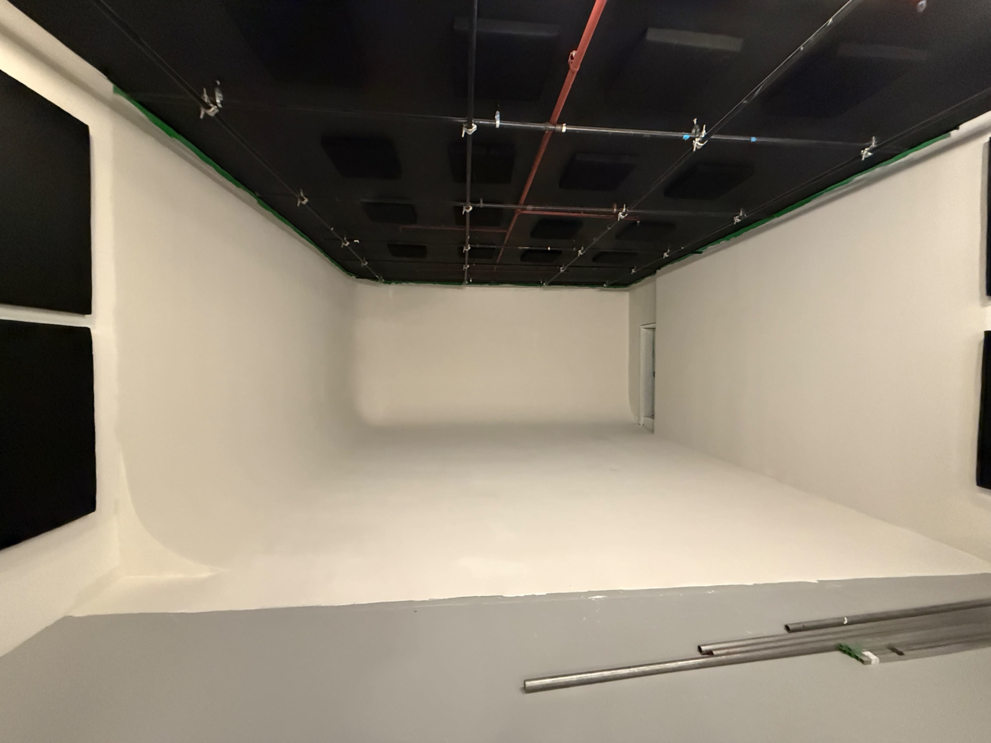 The image shows a spacious studio with white walls, a smooth floor, and soundproofing panels mounted on the ceiling.