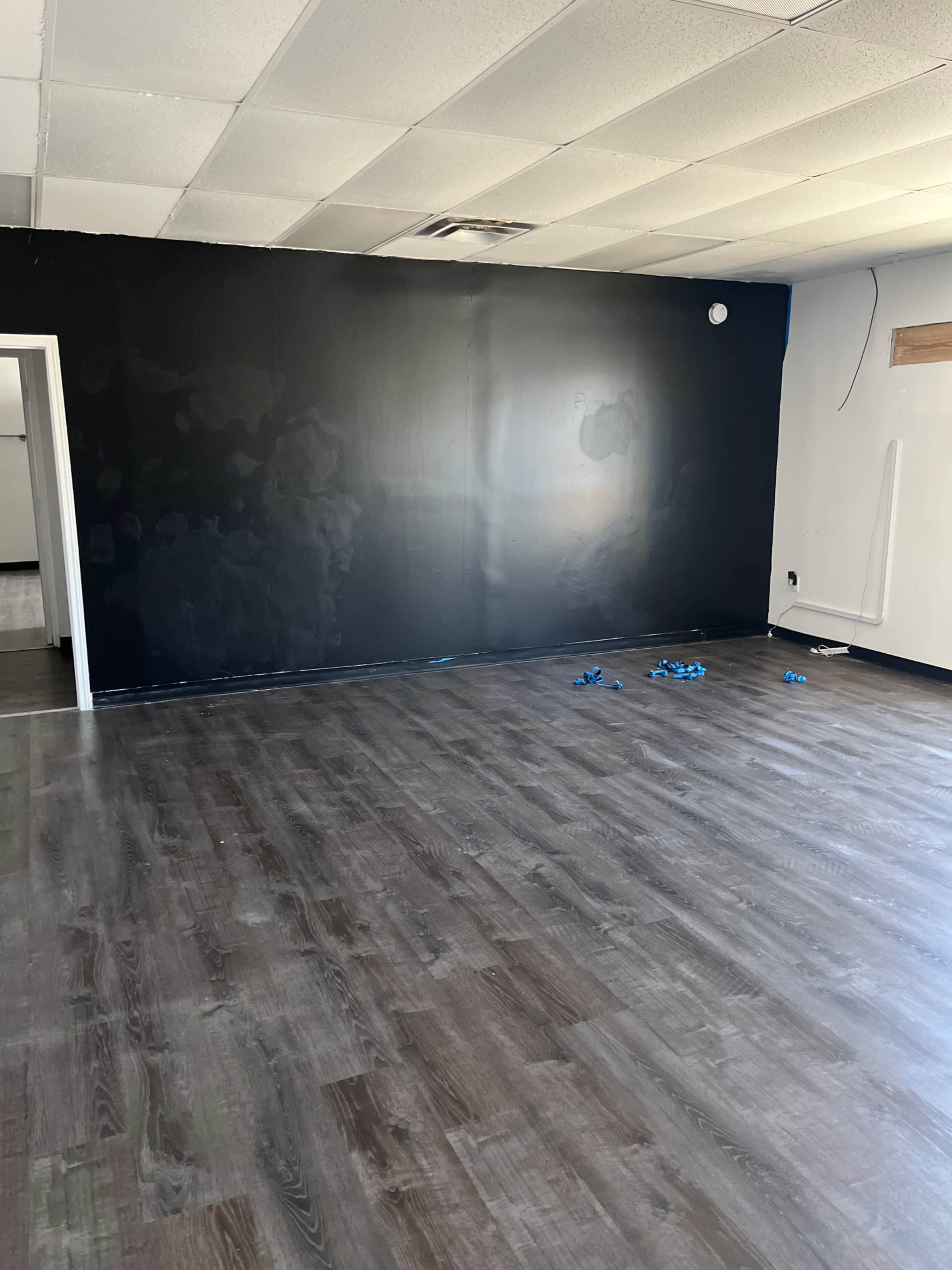 The room features a dark-painted wall and a floor with dark wood laminate, accompanied by some blue painter's tape scattered on the surface.