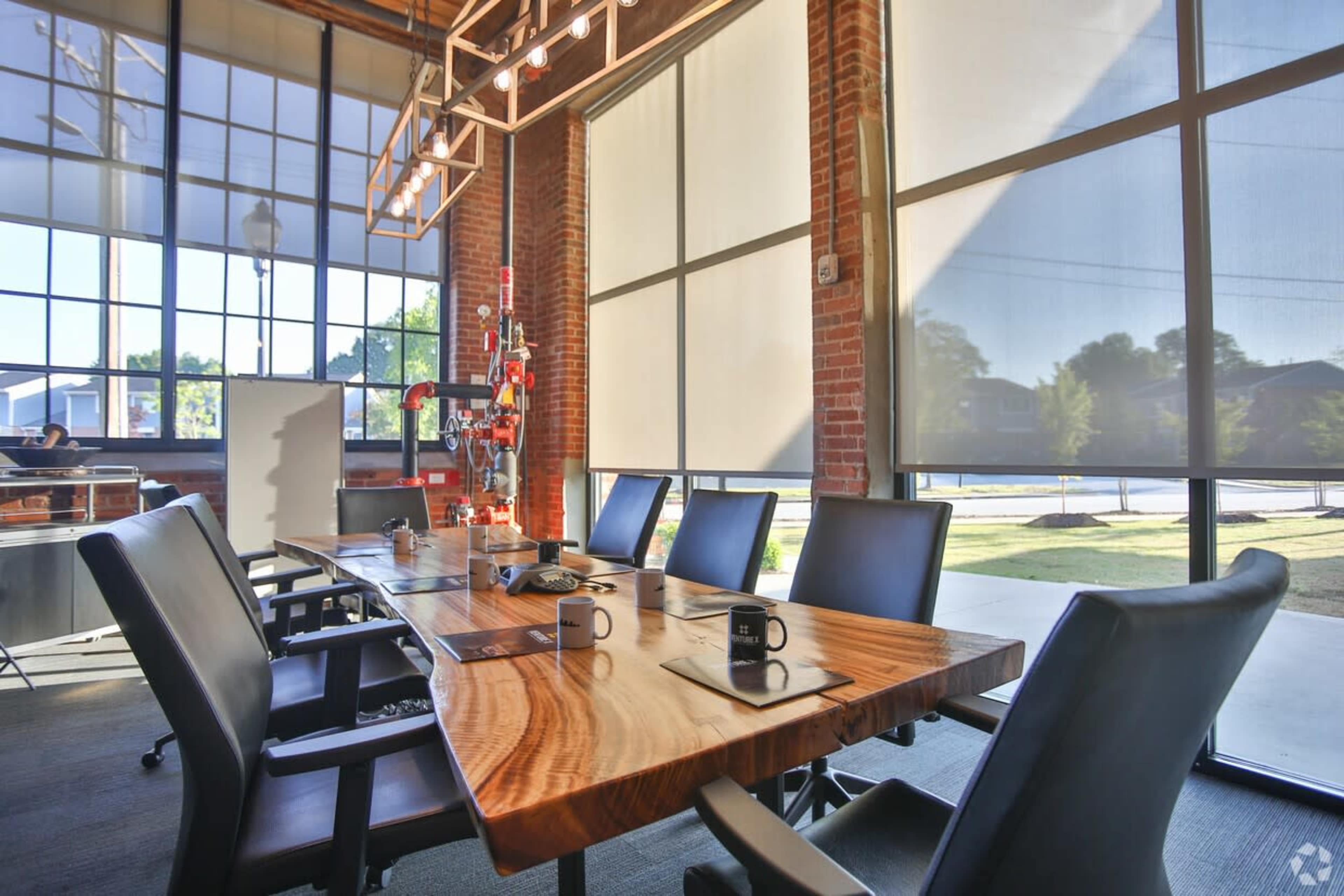 A conference room features a large wooden table surrounded by black chairs, with large windows letting in natural light.
