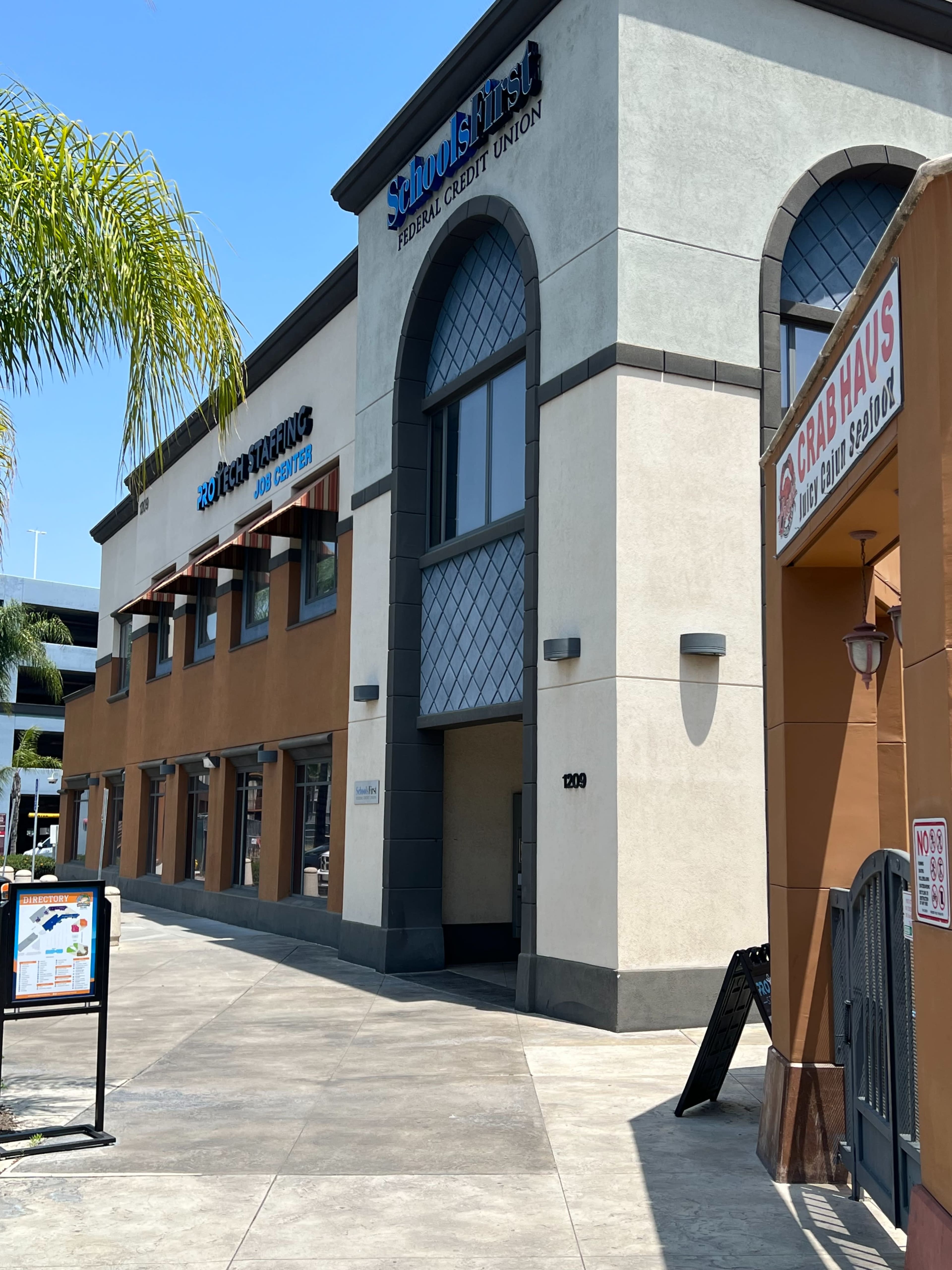 The exterior of a two-story commercial building featuring a credit union and a restaurant, with a sign for "Crab Haus" visible.