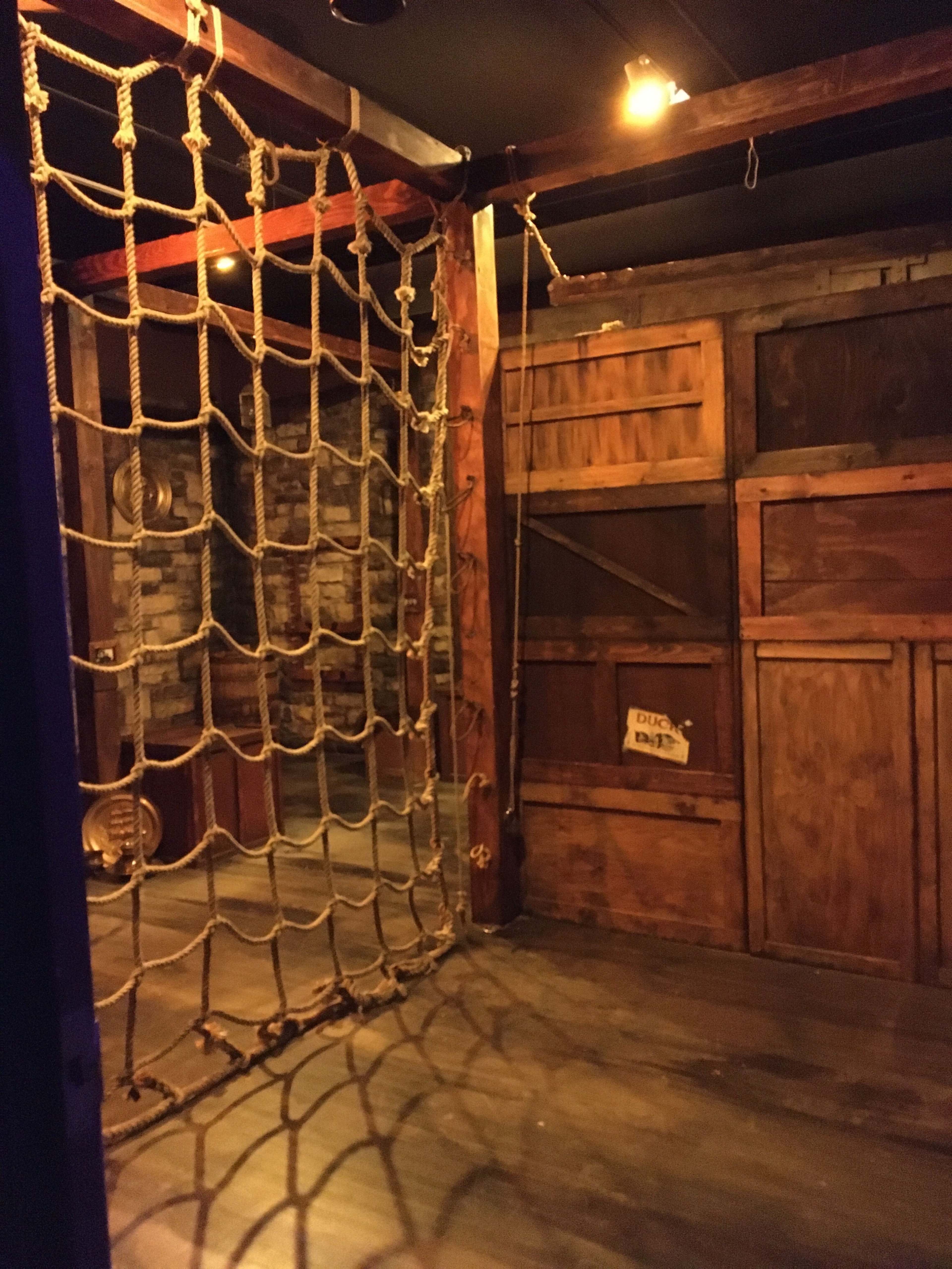 An interior space featuring a wooden structure with a large rope net on one side and wooden panels on the opposite wall.