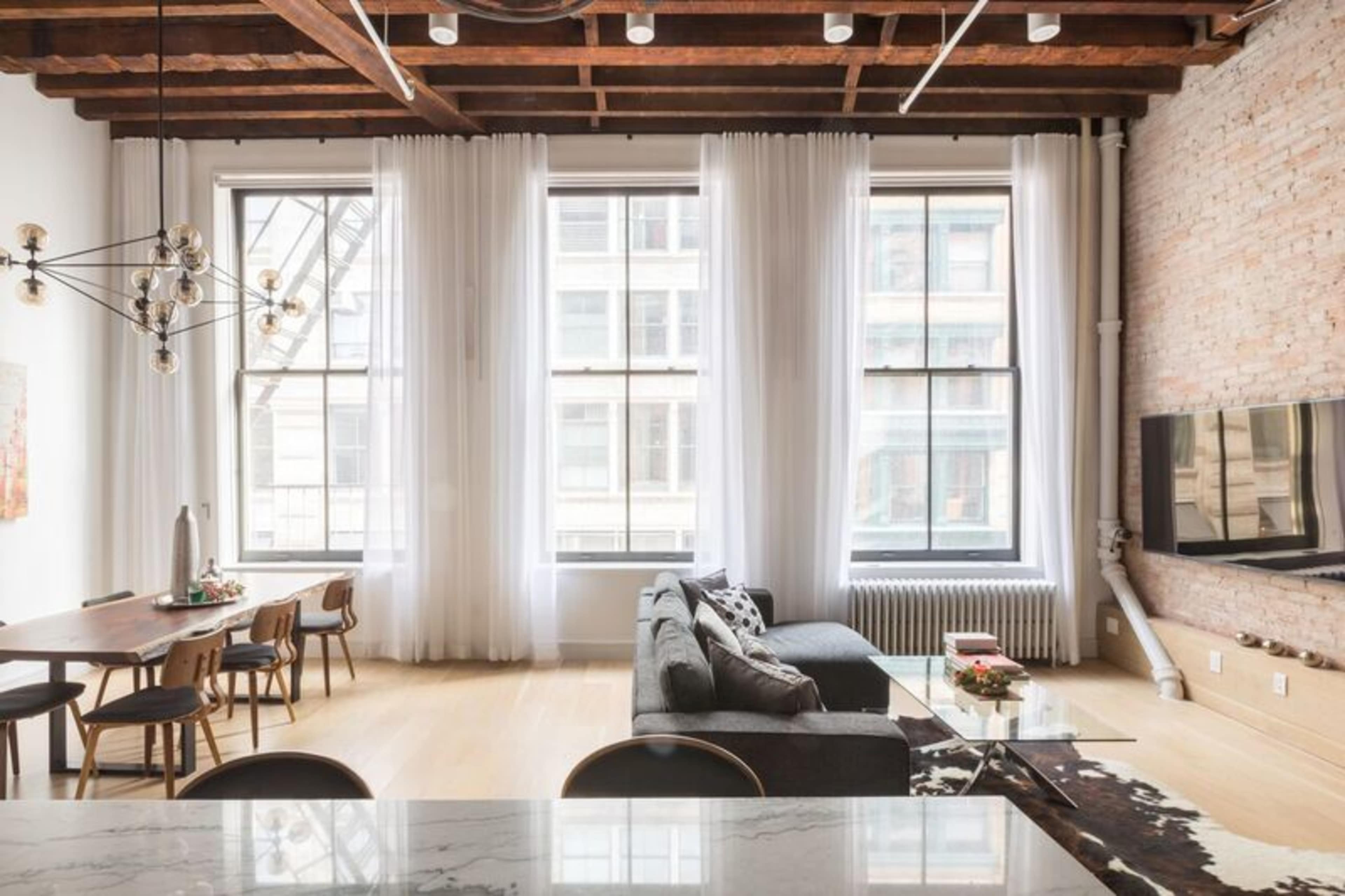 A modern, open-concept living space with large windows, a dining area with a wooden table, and a couch facing a wall-mounted television.