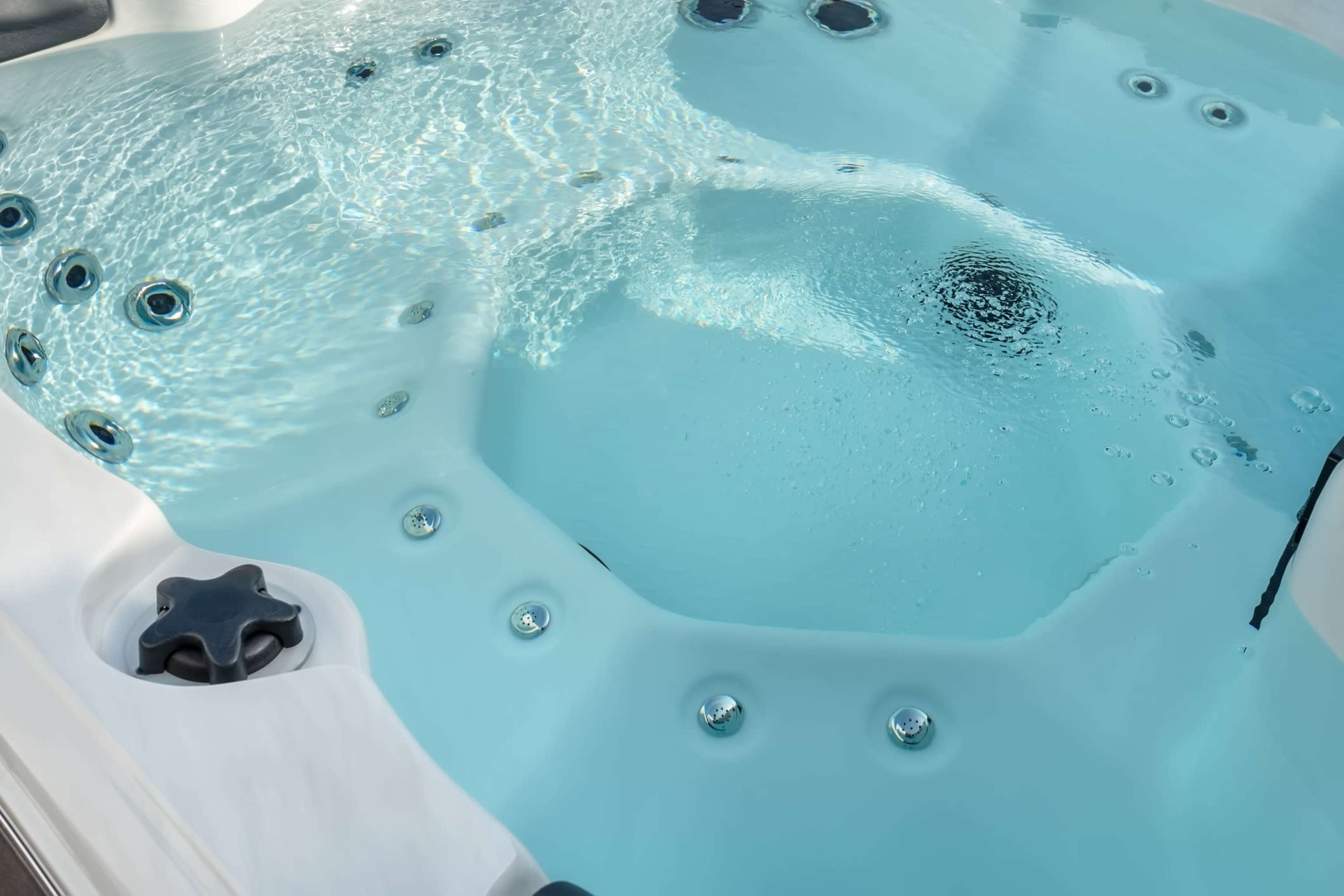 The image shows a hot tub filled with clear water, featuring several jet nozzles along its edges.