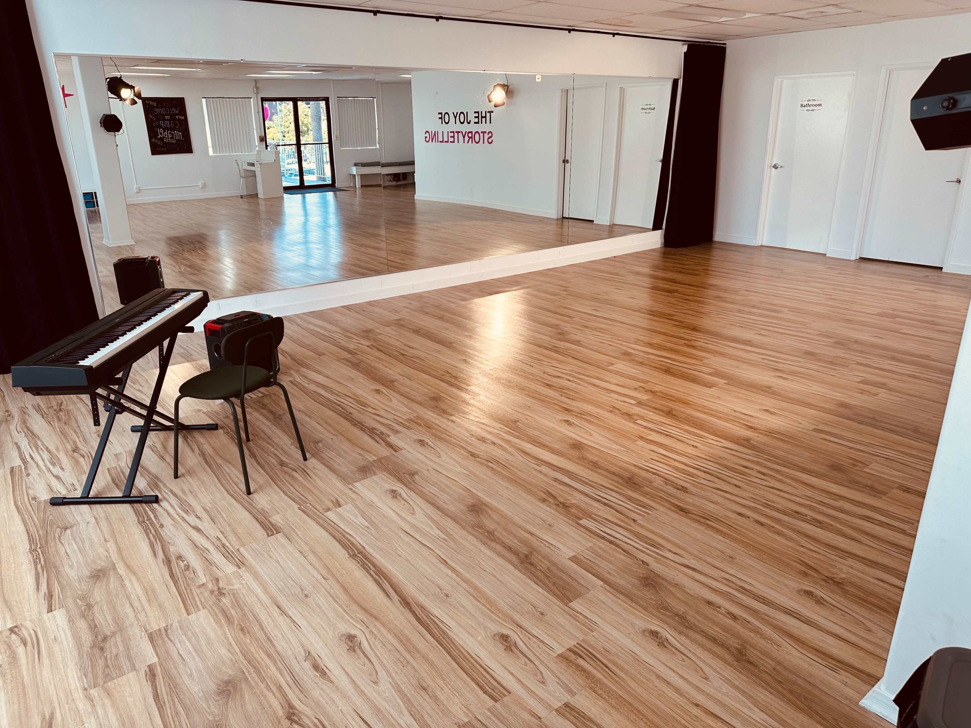 A spacious studio with wooden flooring, a piano keyboard on a stand, and large mirrors along one wall.