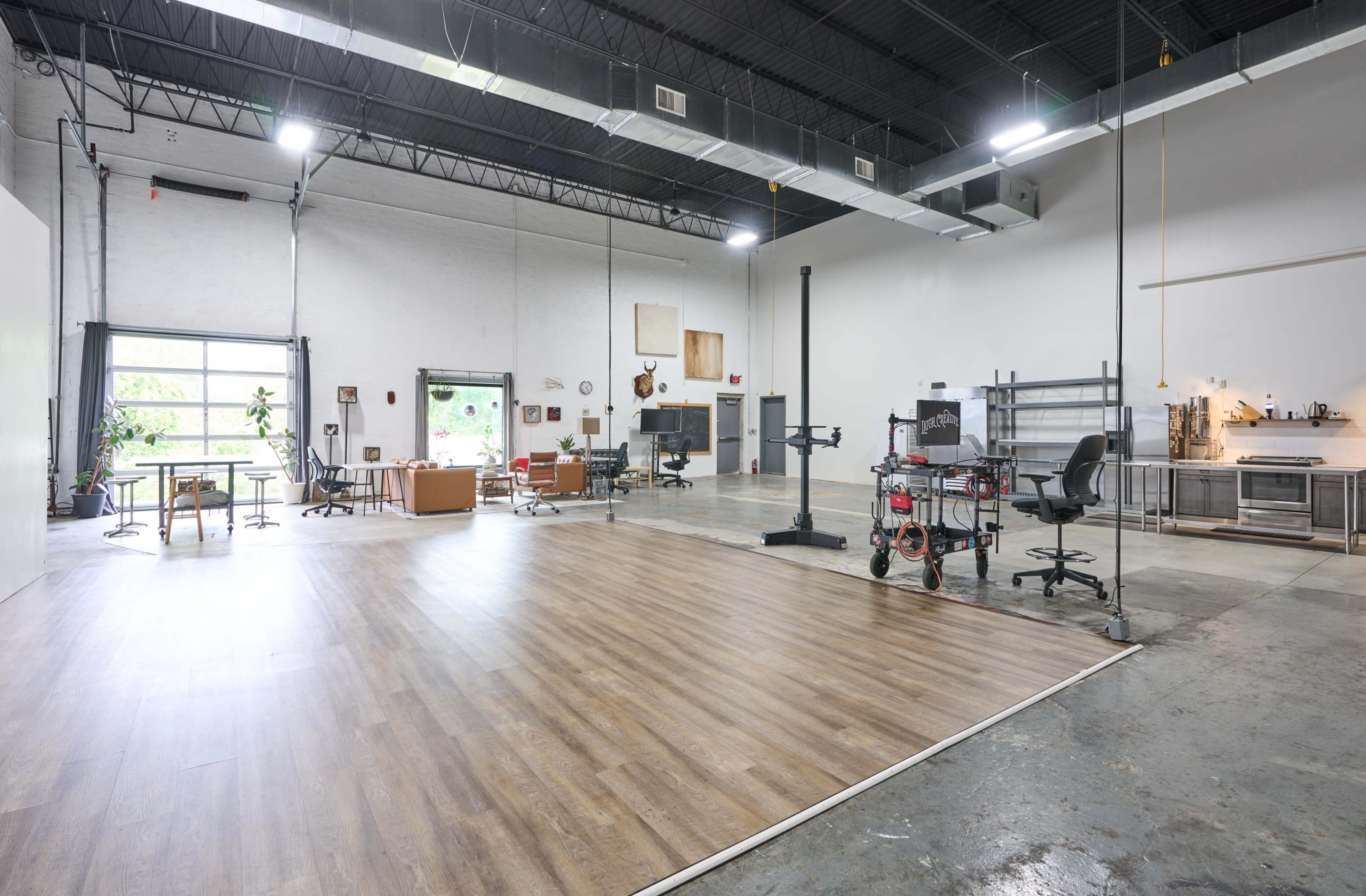 The spacious interior of a modern studio features hardwood flooring, industrial-style fixtures, and areas for seating, workstations, and a kitchenette.