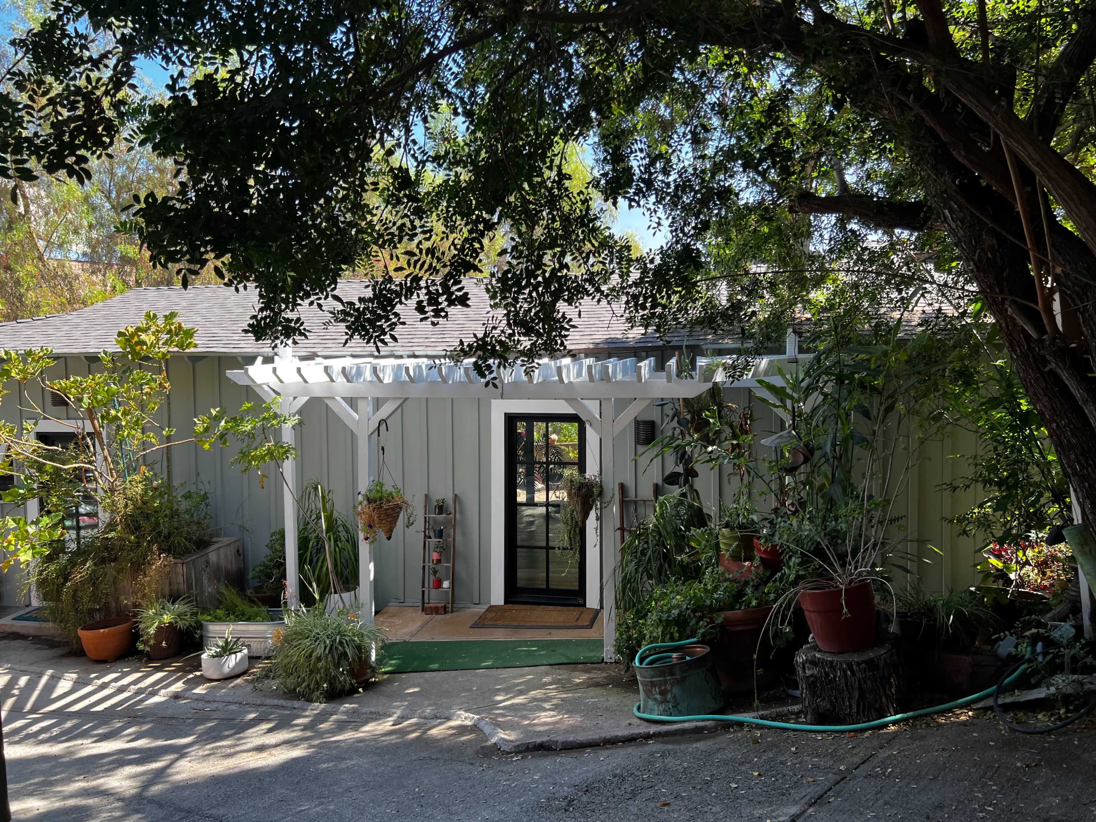 A single-story house with a covered entrance, surrounded by various potted plants and greenery.
