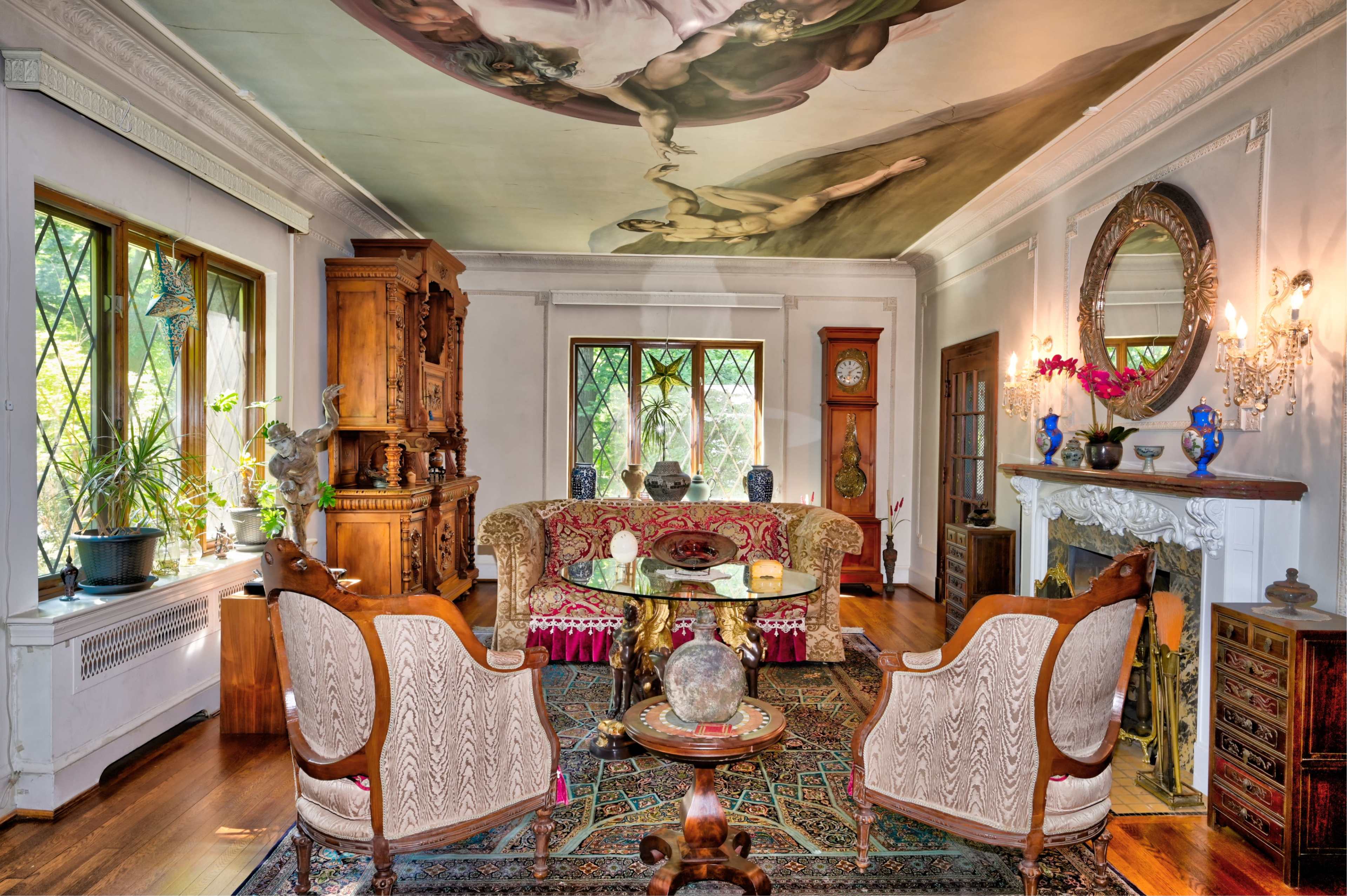 A living room with ornate furniture, a decorative ceiling mural, and a fireplace surrounded by various decor items.