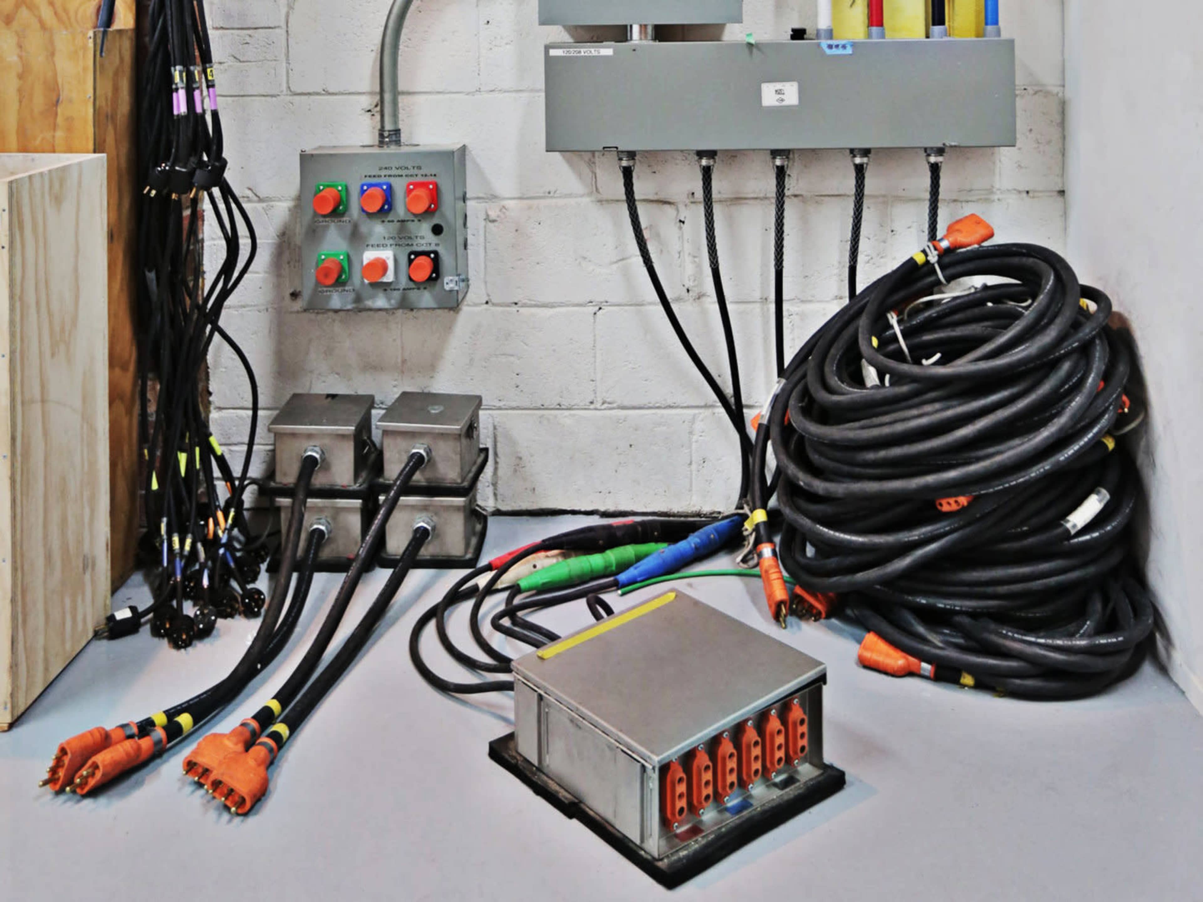 The image shows a collection of electrical cables and distribution boxes arranged against a concrete wall.