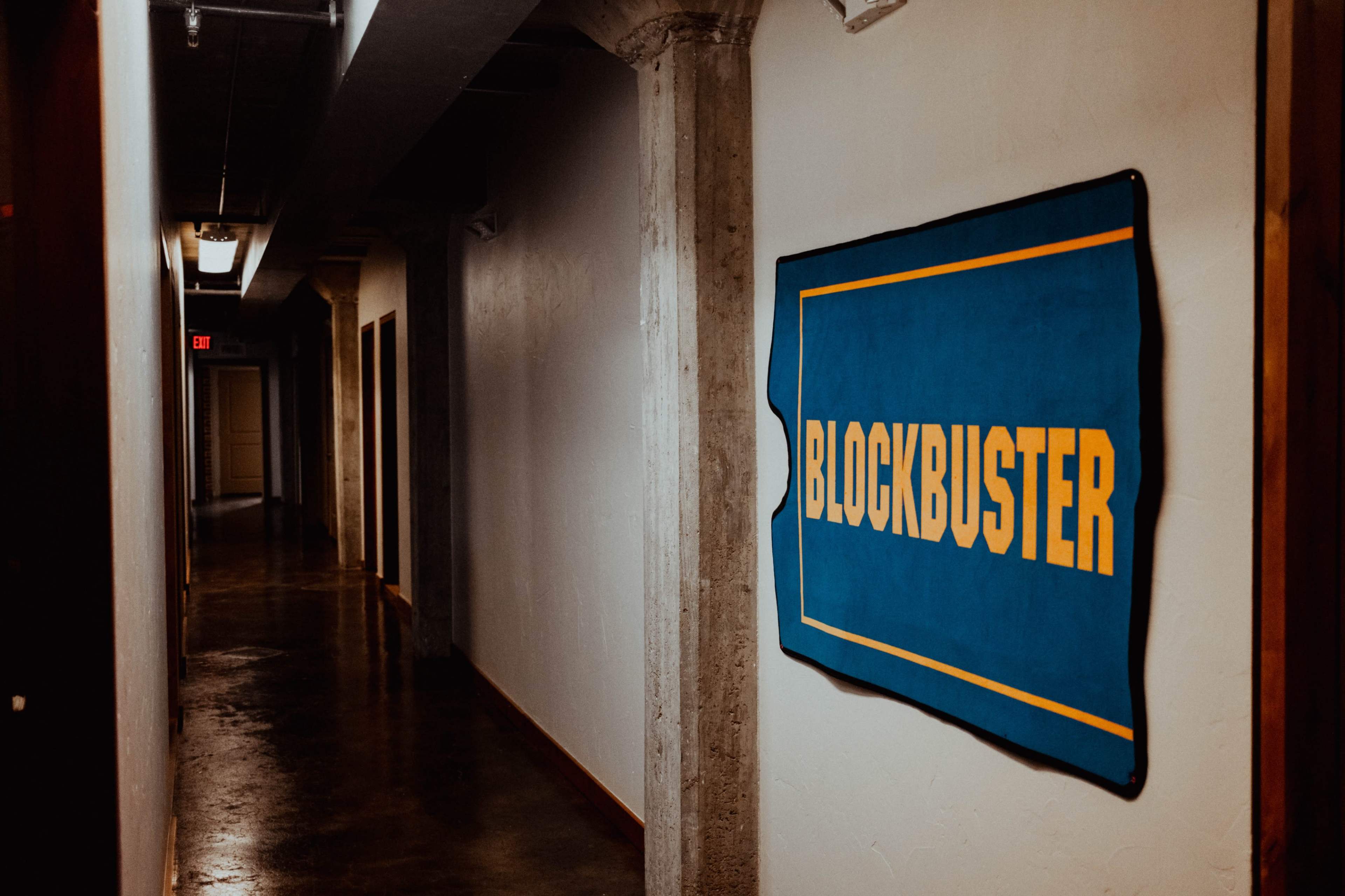 The image shows a dimly lit hallway with a blue and yellow Blockbuster sign mounted on a wall.