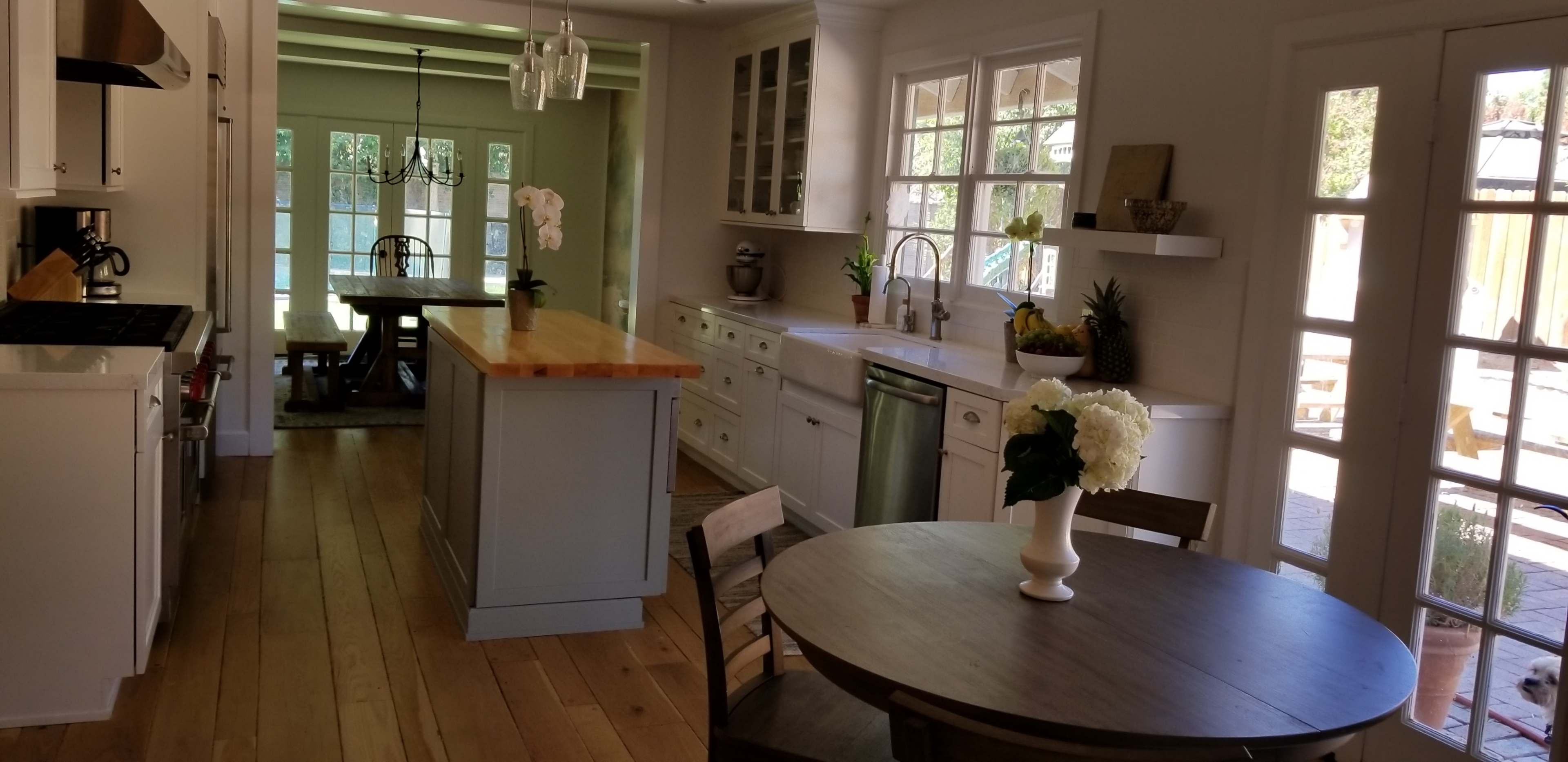 A spacious kitchen features a central island, a round dining table, large windows, and light-colored cabinetry.