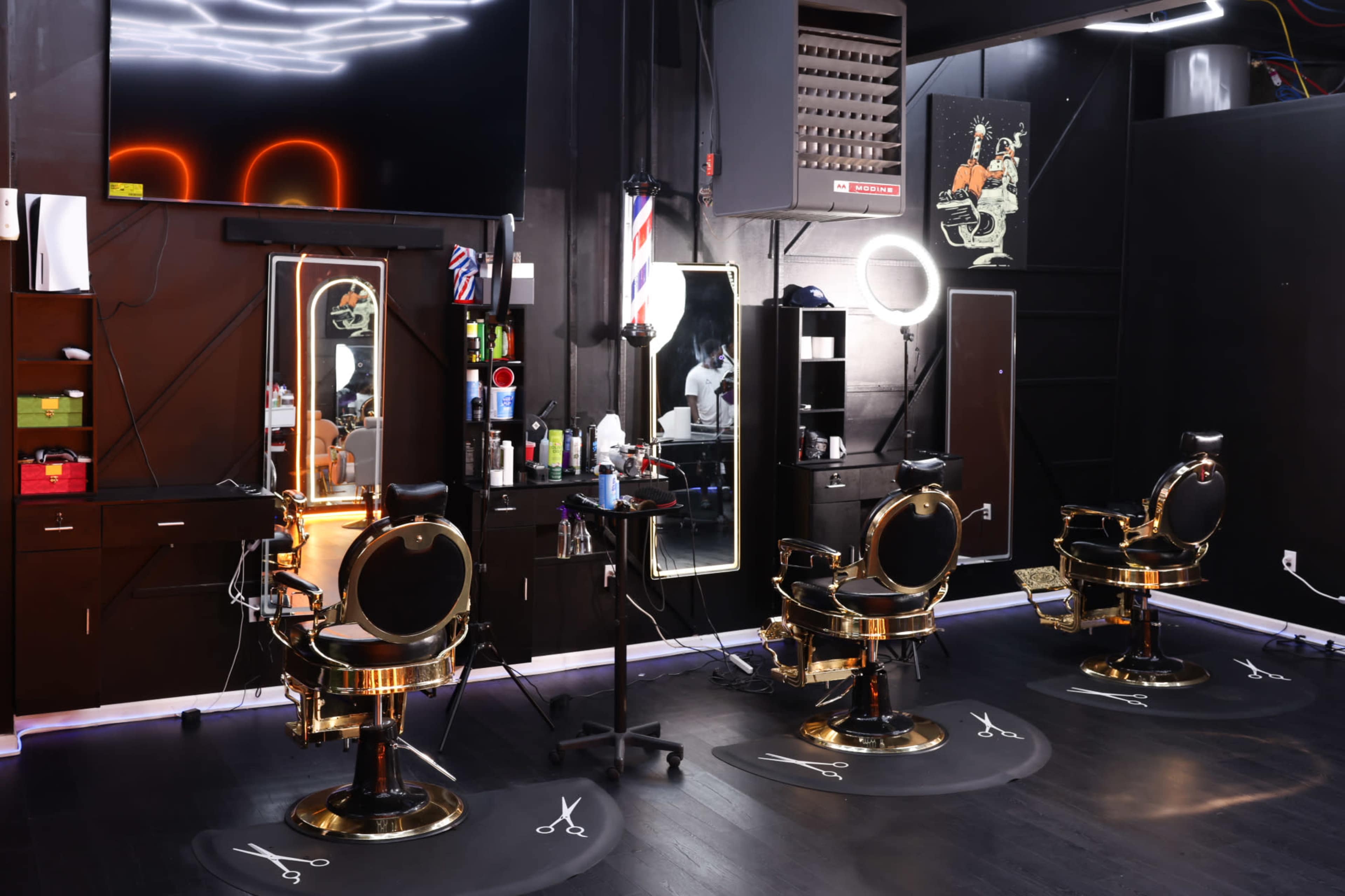 The image shows a modern barbershop interior featuring three gold and black barber chairs arranged around mirrored stations with various grooming products on the shelves.