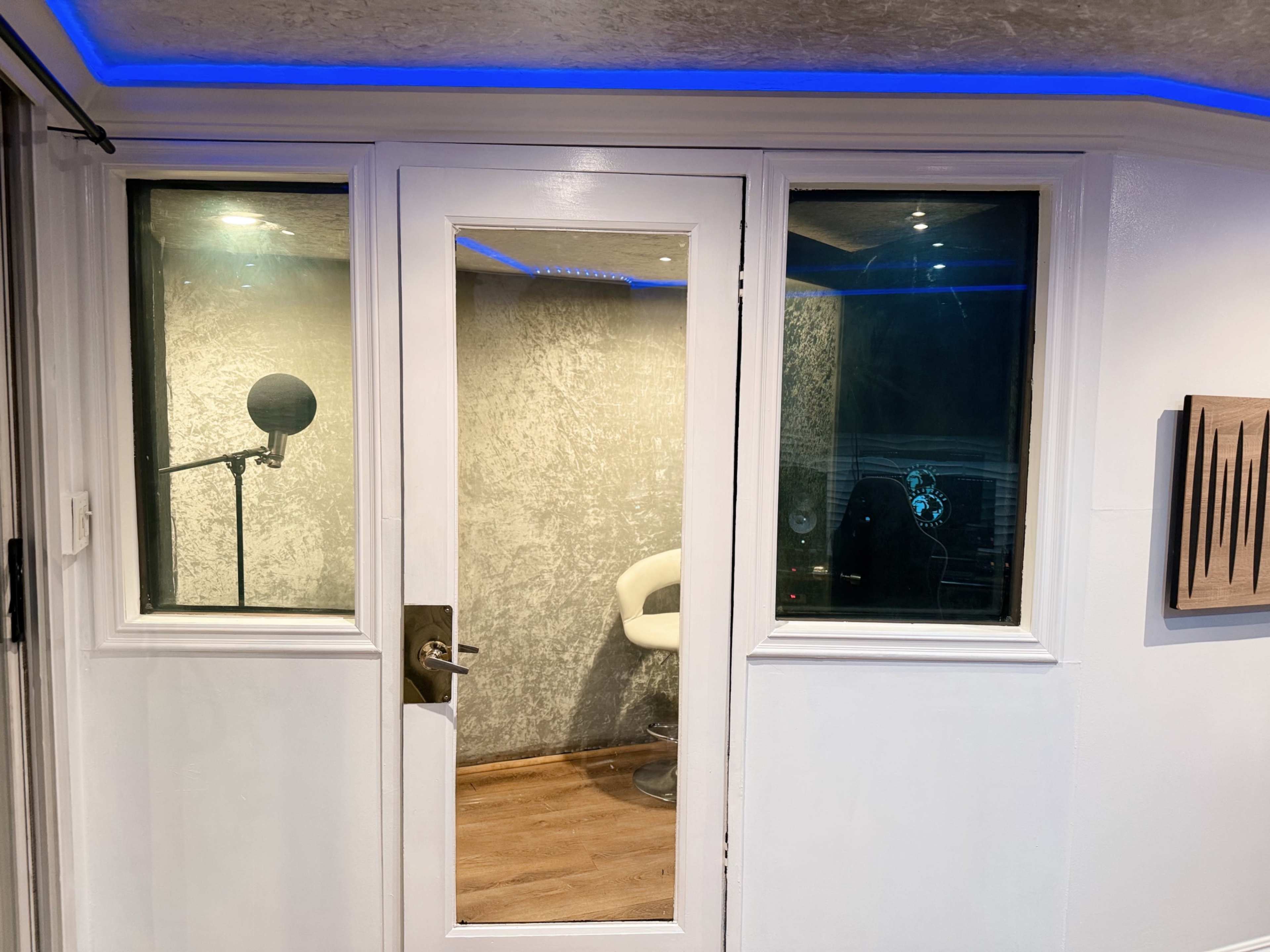 The image shows a soundproof recording studio with a glass door, a microphone on a stand, and a chair inside.