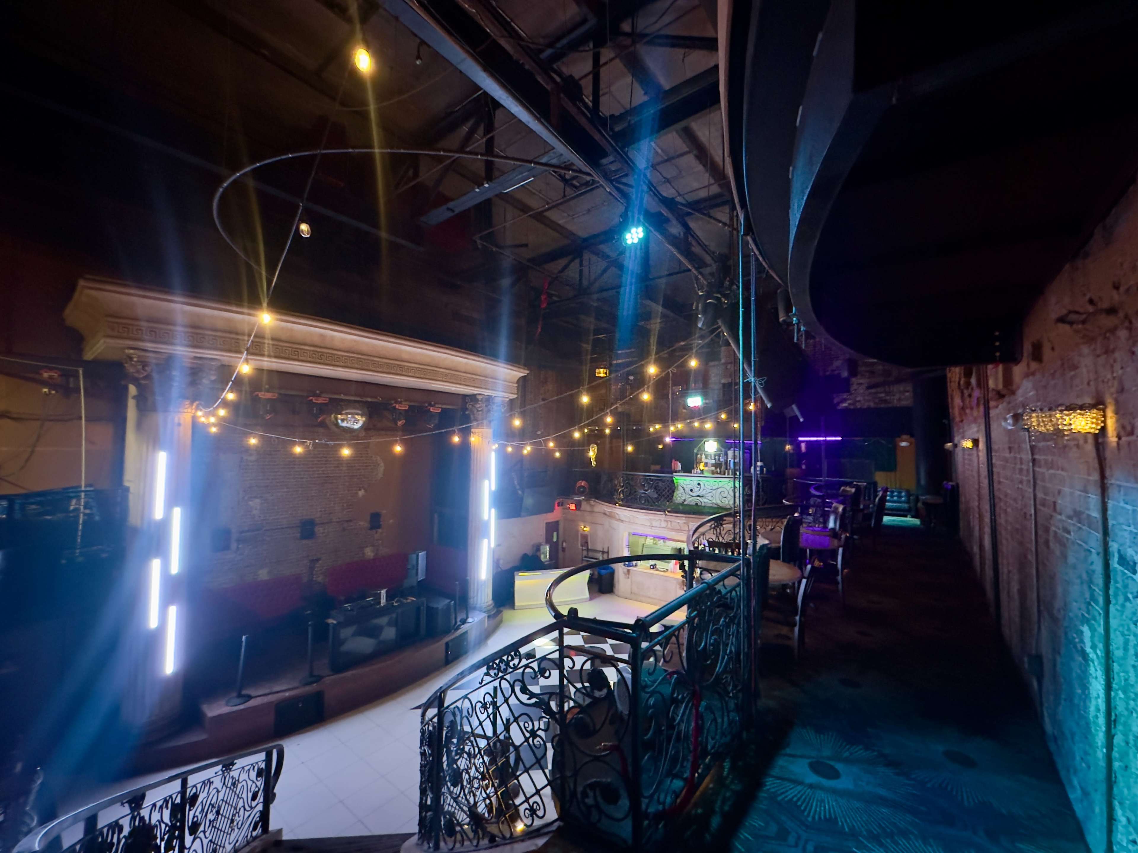 The image shows an empty nightclub interior featuring a dance floor, colorful lighting, and a decorative railing overlooking the space.