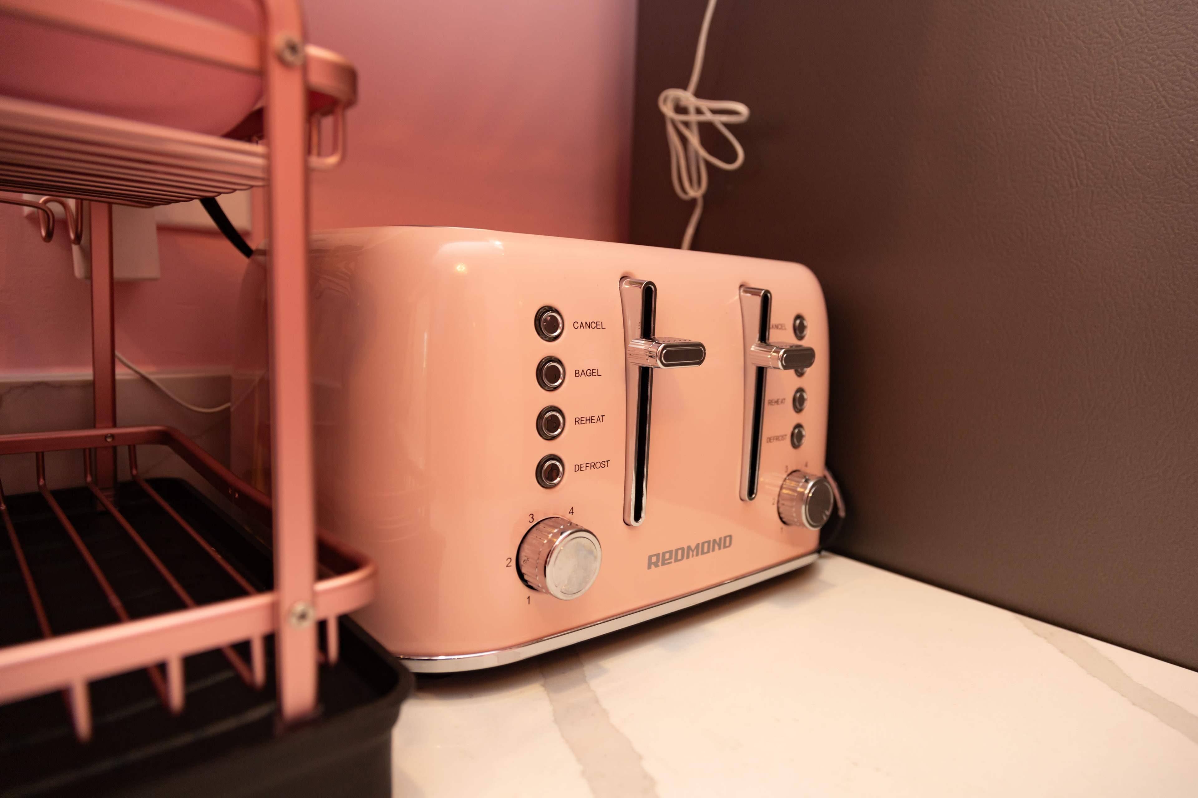 A pink toaster positioned on a countertop next to a wire storage shelf.