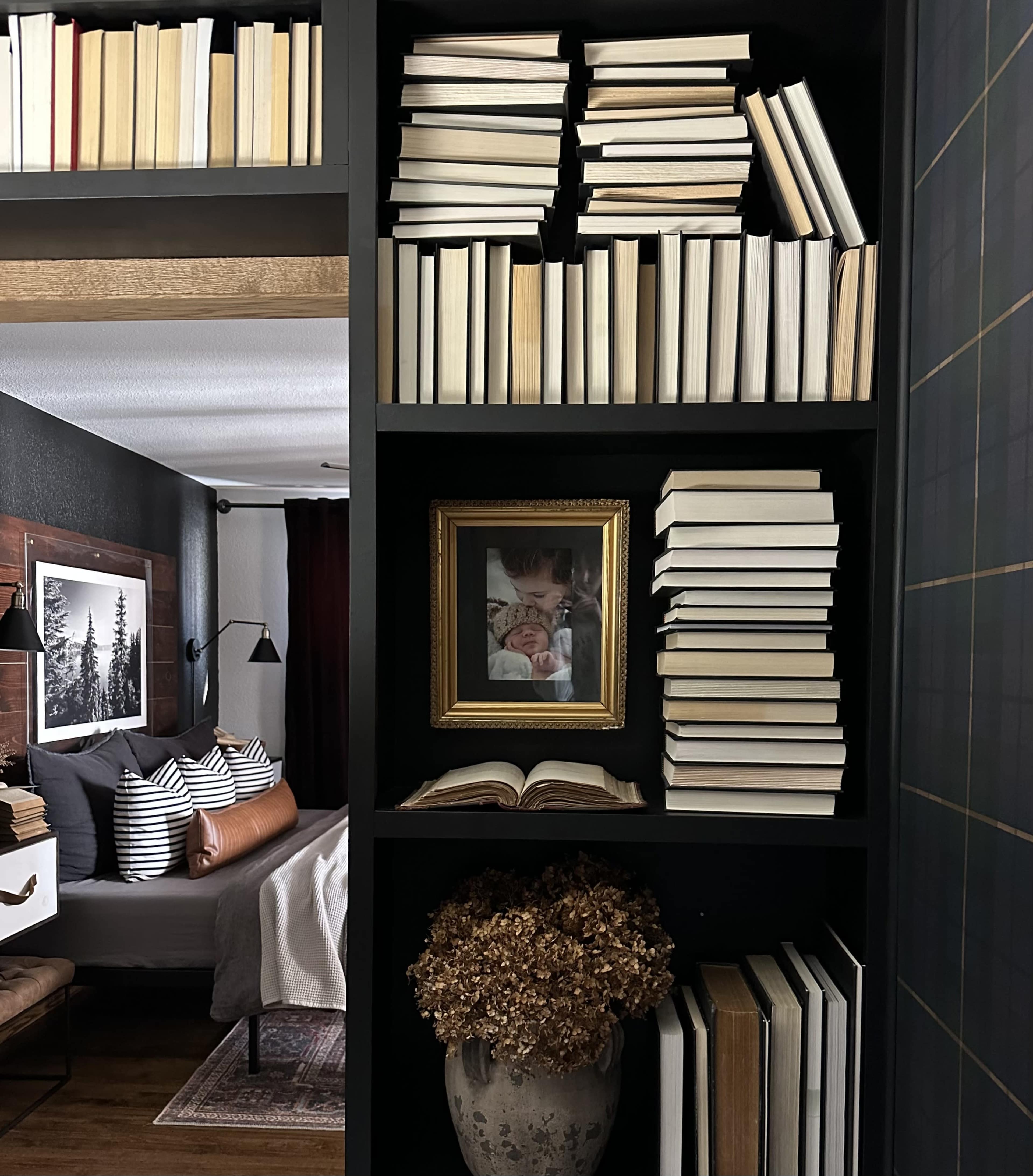 A bookshelf filled with neatly stacked books and a framed photo, positioned near a bed in a cozy room.