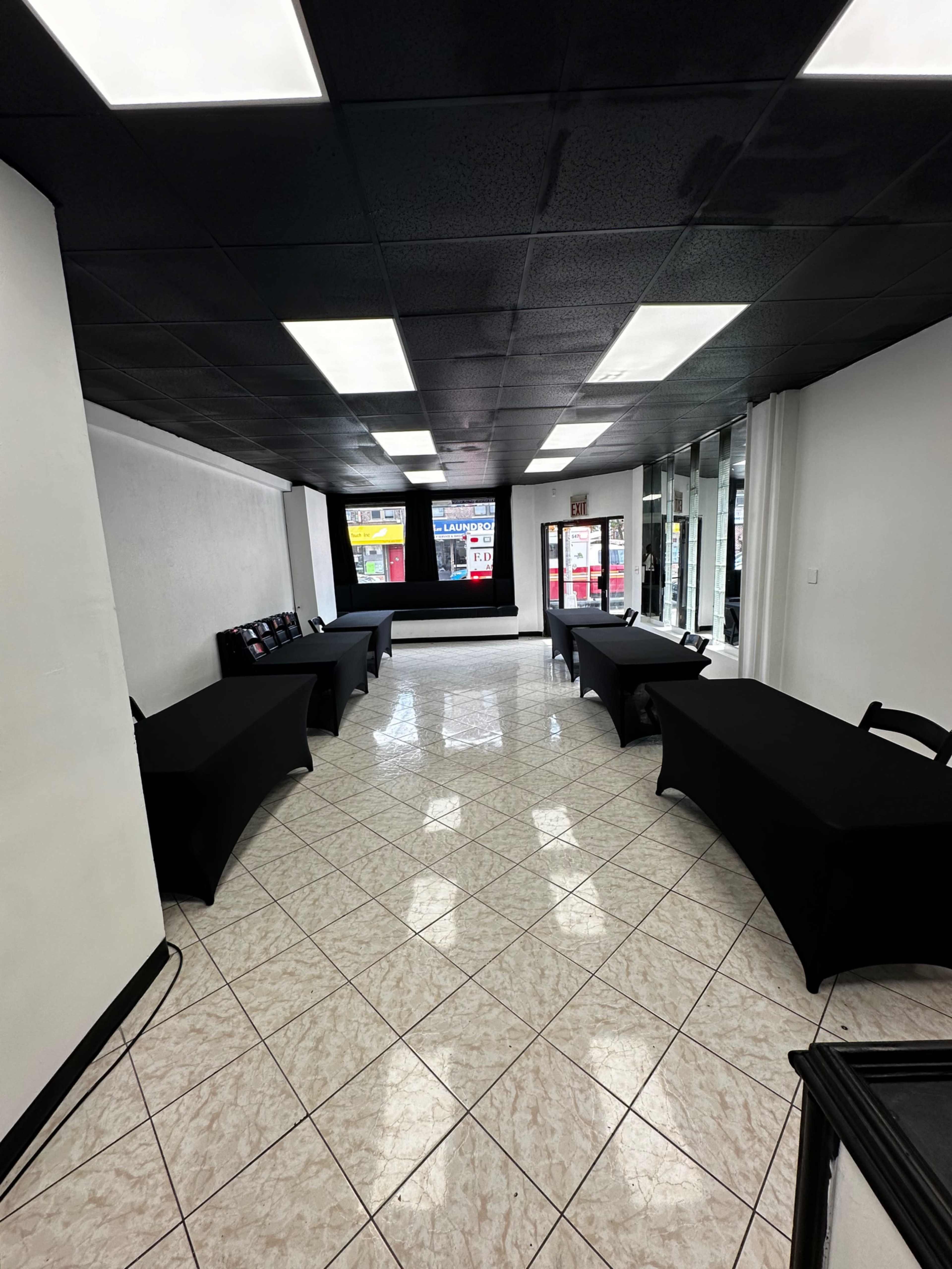 The image shows a spacious room with black-covered tables arranged in a line and tile flooring.