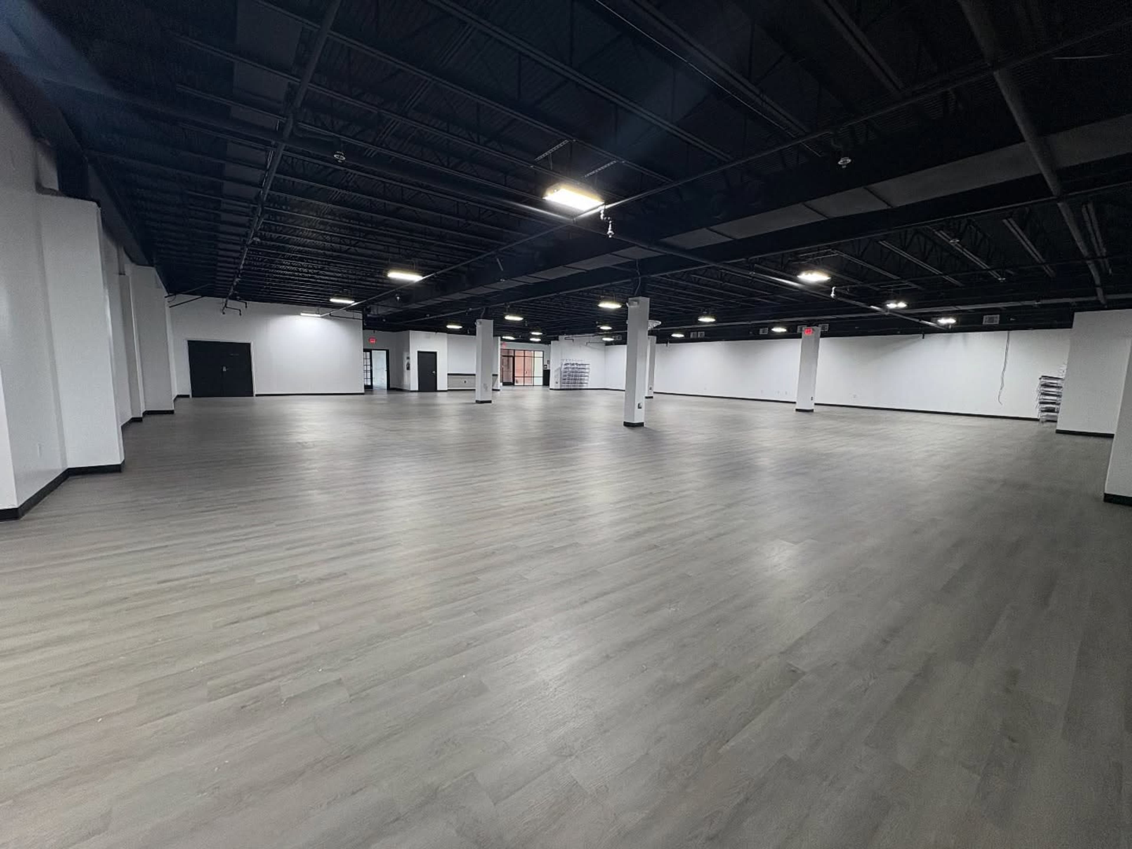 The image shows a large, empty commercial space with a smooth gray floor and white walls.