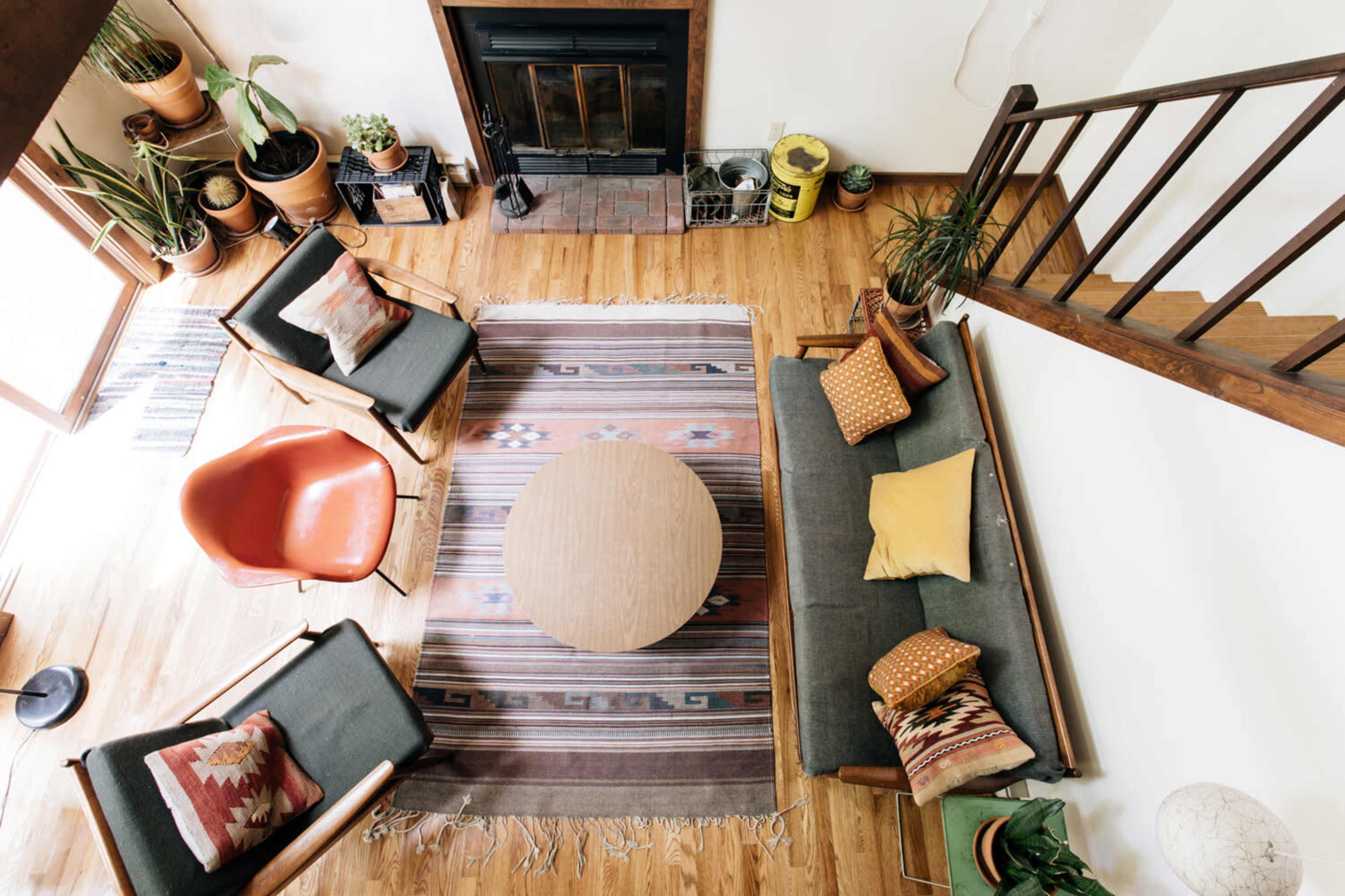The image shows a cozy living room with a wooden floor, a round coffee table in the center, and comfortable seating arranged around a patterned rug.