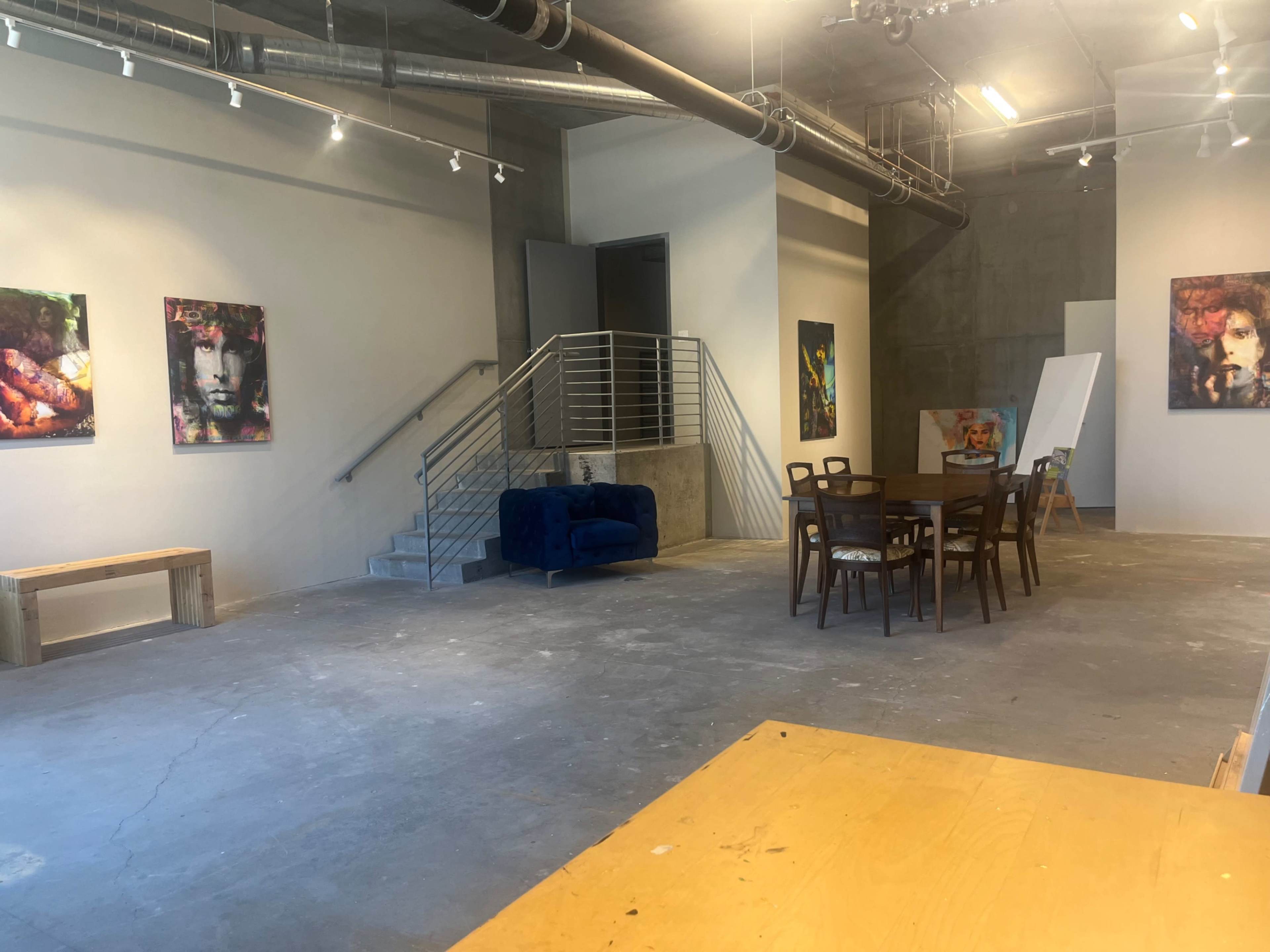 A spacious, minimalist room with artwork on the walls, a staircase, a blue couch, and a long wooden dining table surrounded by chairs.