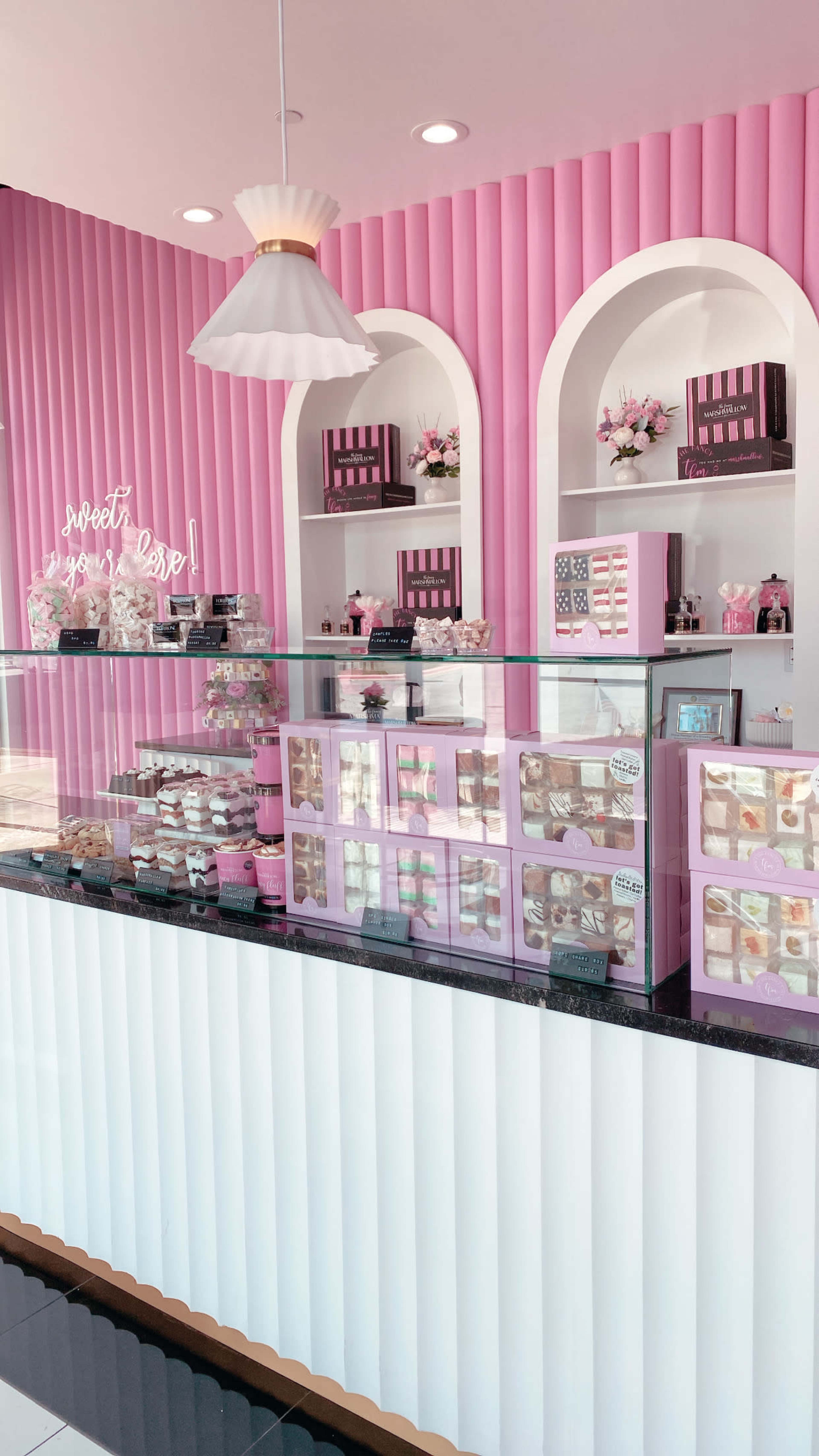 A bakery display with a pink and white interior, featuring an assortment of colorful desserts and pastries in glass cases.