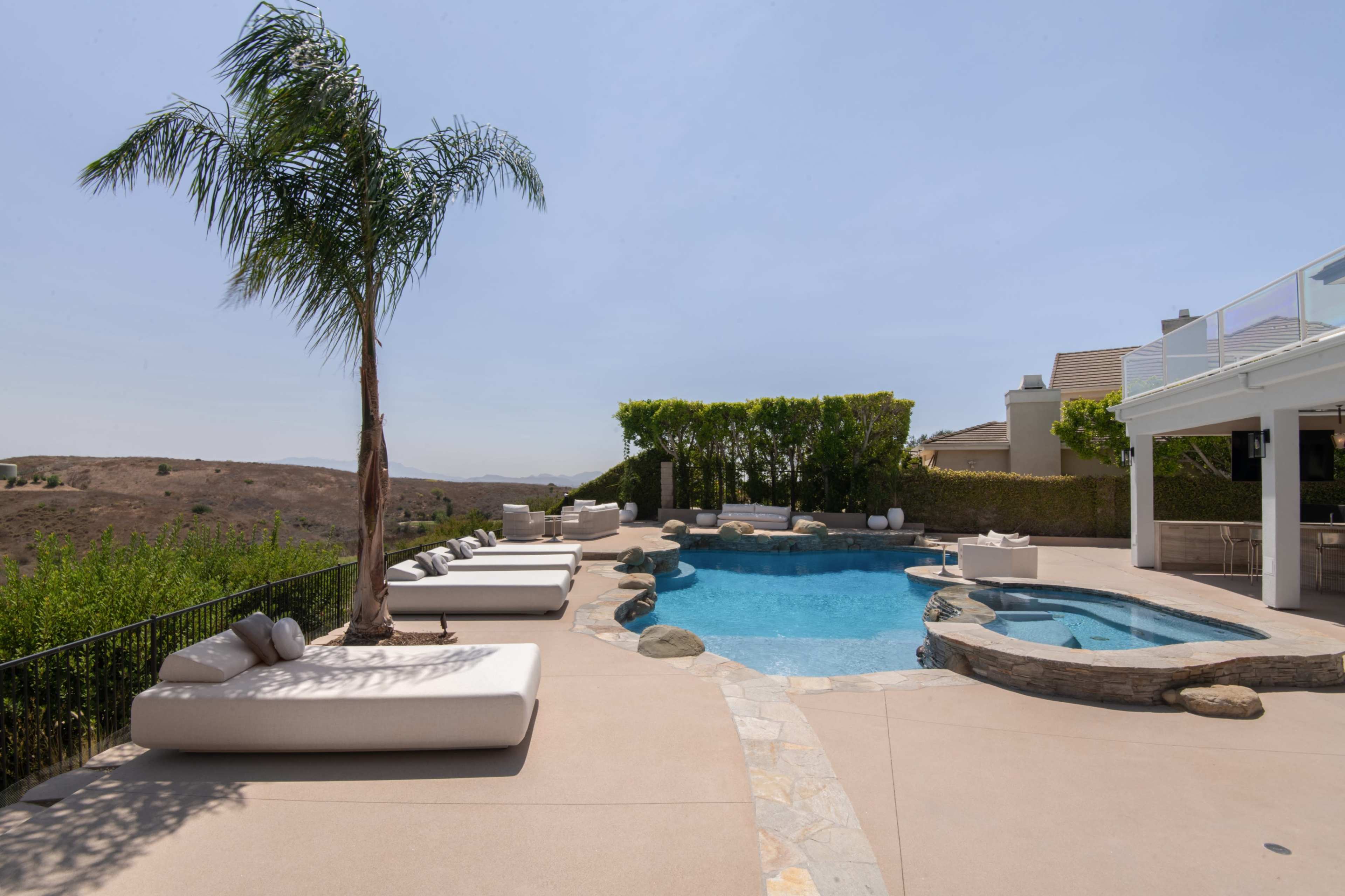 The image shows a pool area with lounge chairs, a palm tree, and a landscaped view of rolling hills.