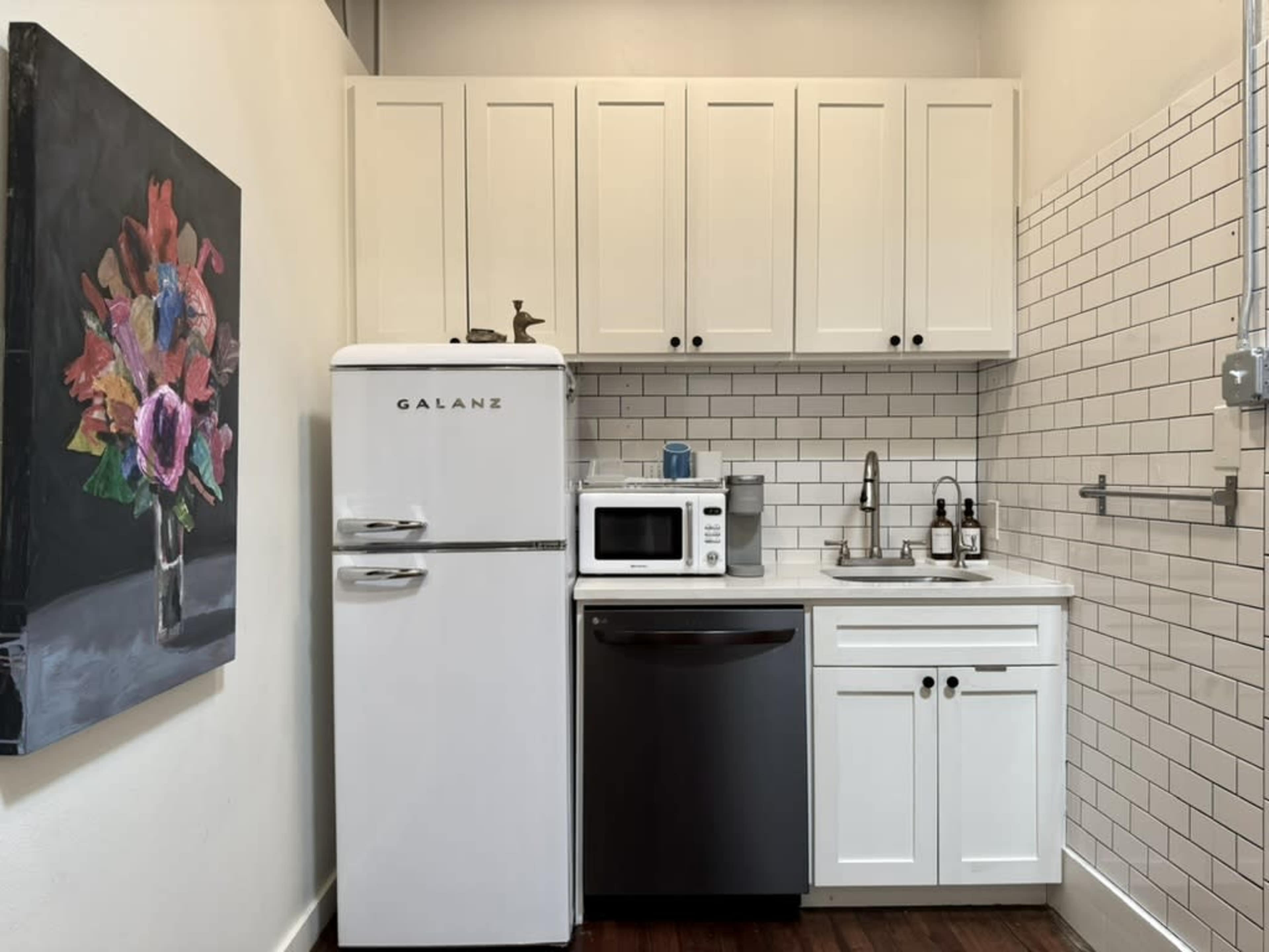 The image shows a compact kitchen featuring a white Galanz refrigerator, a microwave, a stainless steel dishwasher, and white cabinets with a tiled backsplash.