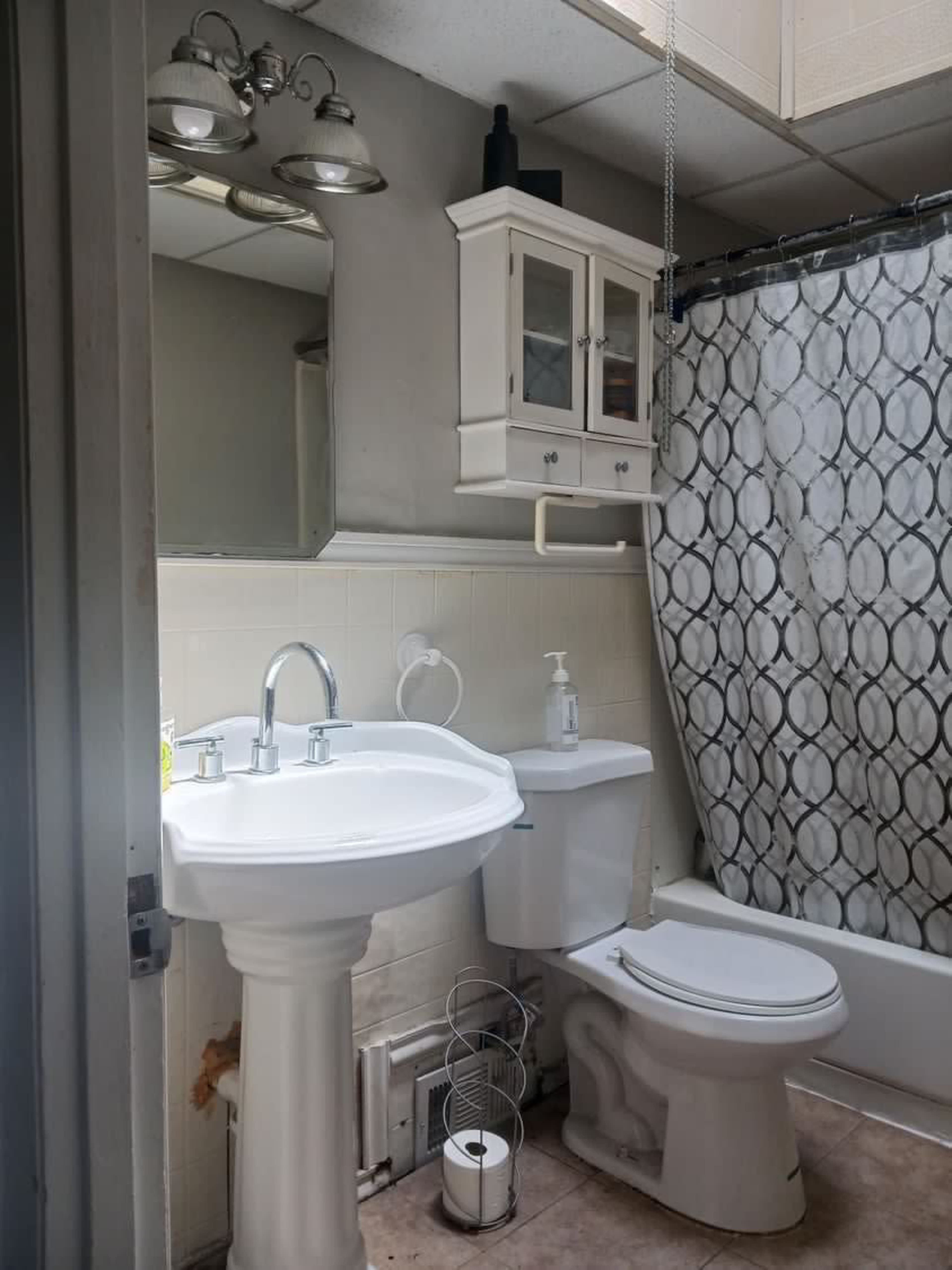 A small bathroom featuring a white sink with a chrome faucet, a toilet, a shower with a patterned curtain, and a mirrored cabinet above the sink.