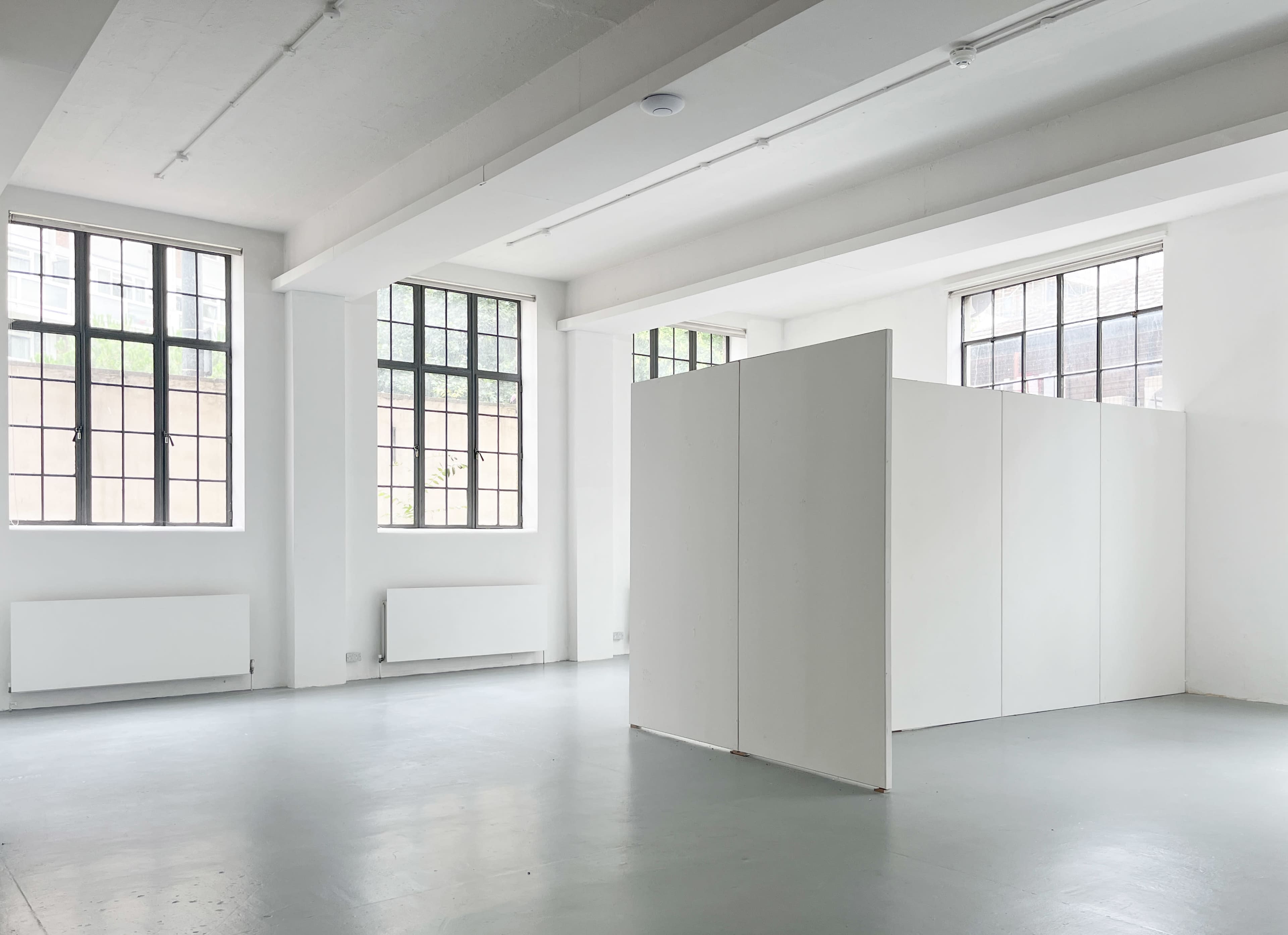 A spacious, minimalist room with white walls, large windows, and a partition dividing the space.