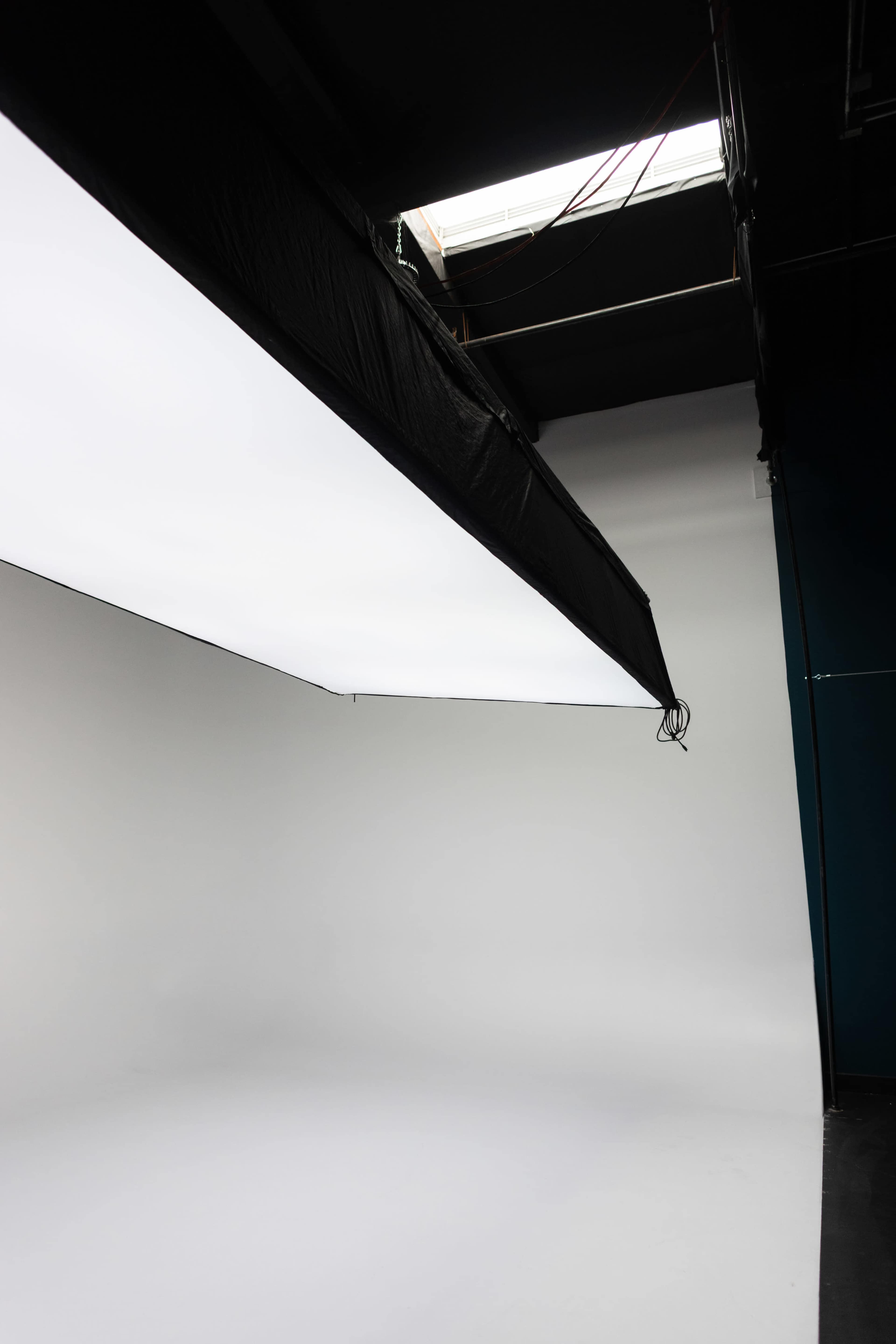 The image shows a photography studio with a large softbox hanging from the ceiling, illuminating a white backdrop.