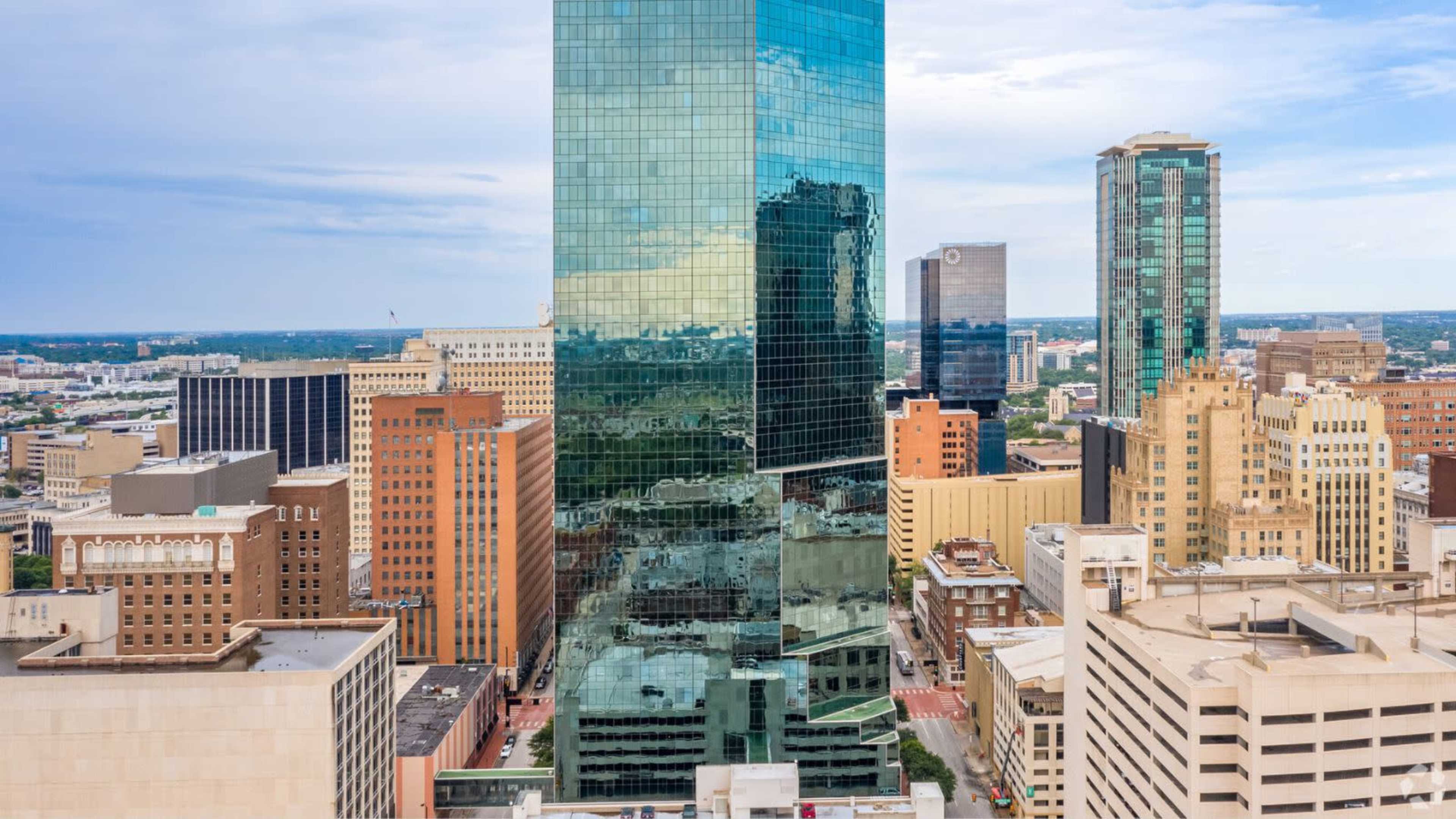 A cluster of tall buildings is visible in a downtown area, with a reflective glass tower dominating the scene.