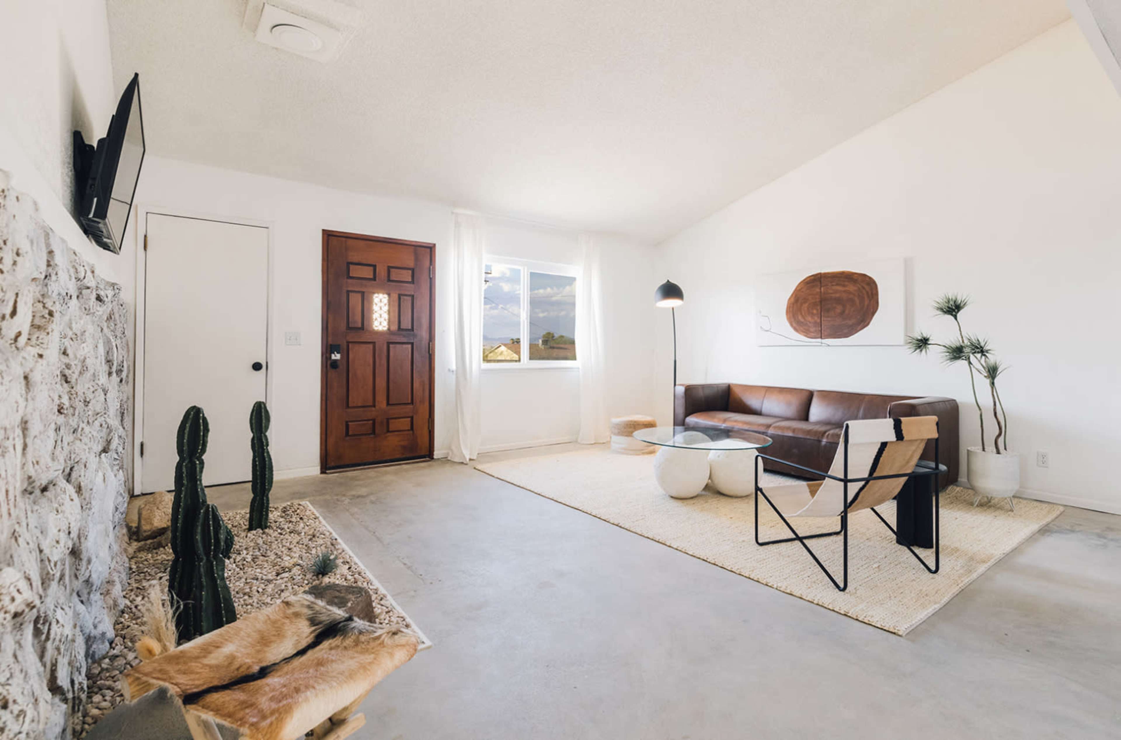 A modern living room with a brown leather sofa, a glass coffee table, and a door leading to the outside.