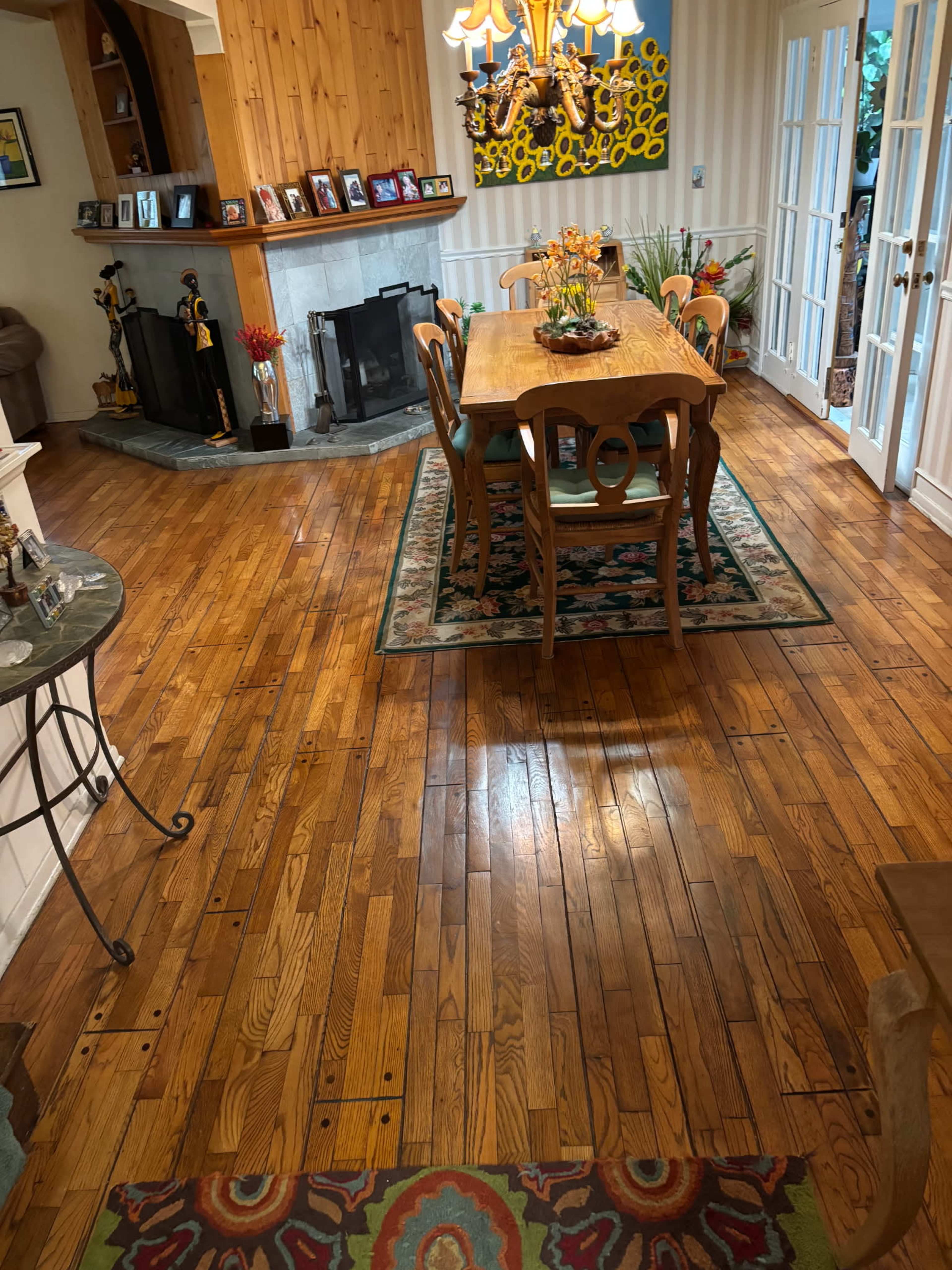 The image shows a spacious dining area with a wooden table and chairs, surrounded by hardwood flooring and a fireplace in the corner.