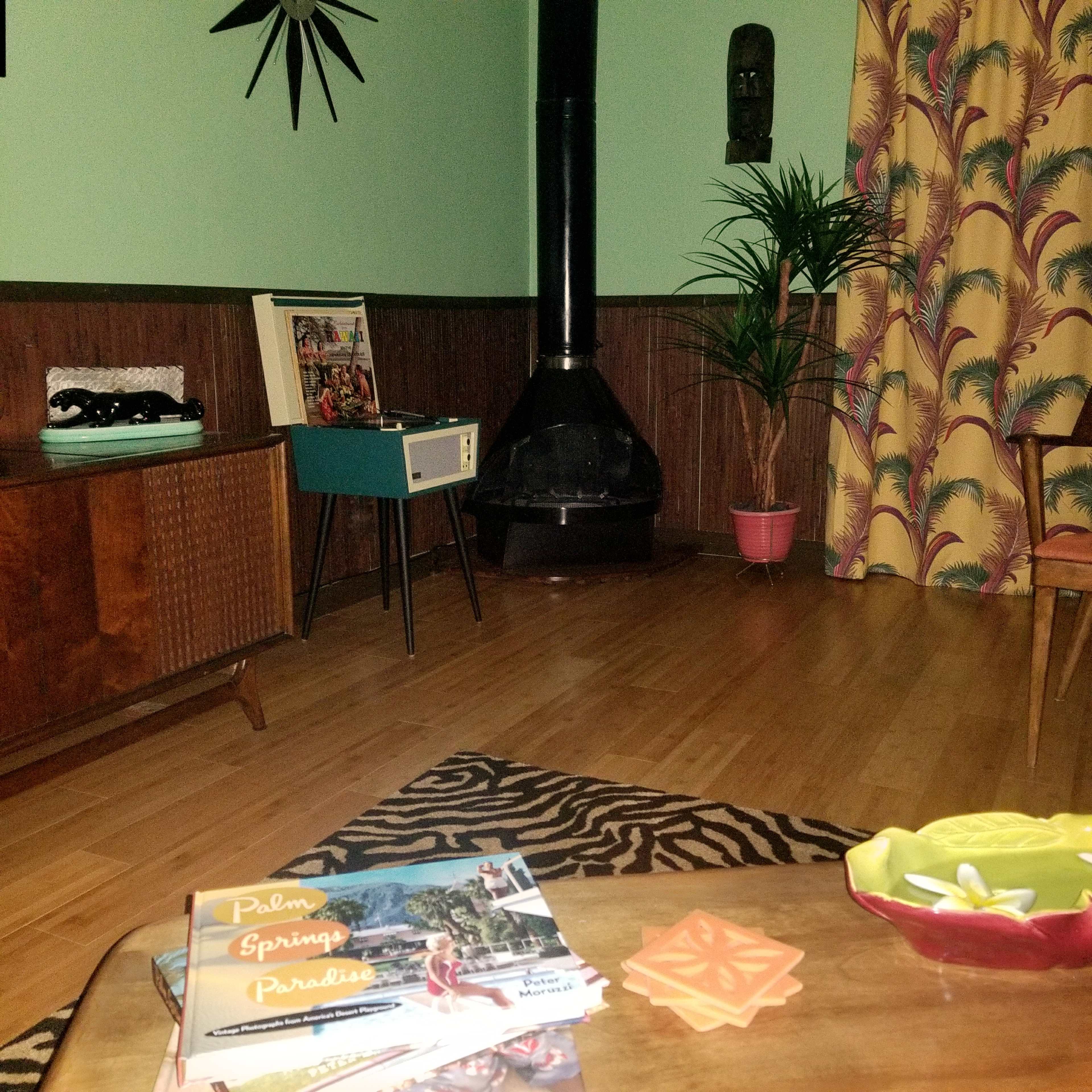 The image showcases a mid-century modern living room featuring a vintage record player, a plant, and patterned curtains, with magazines displayed on a coffee table.
