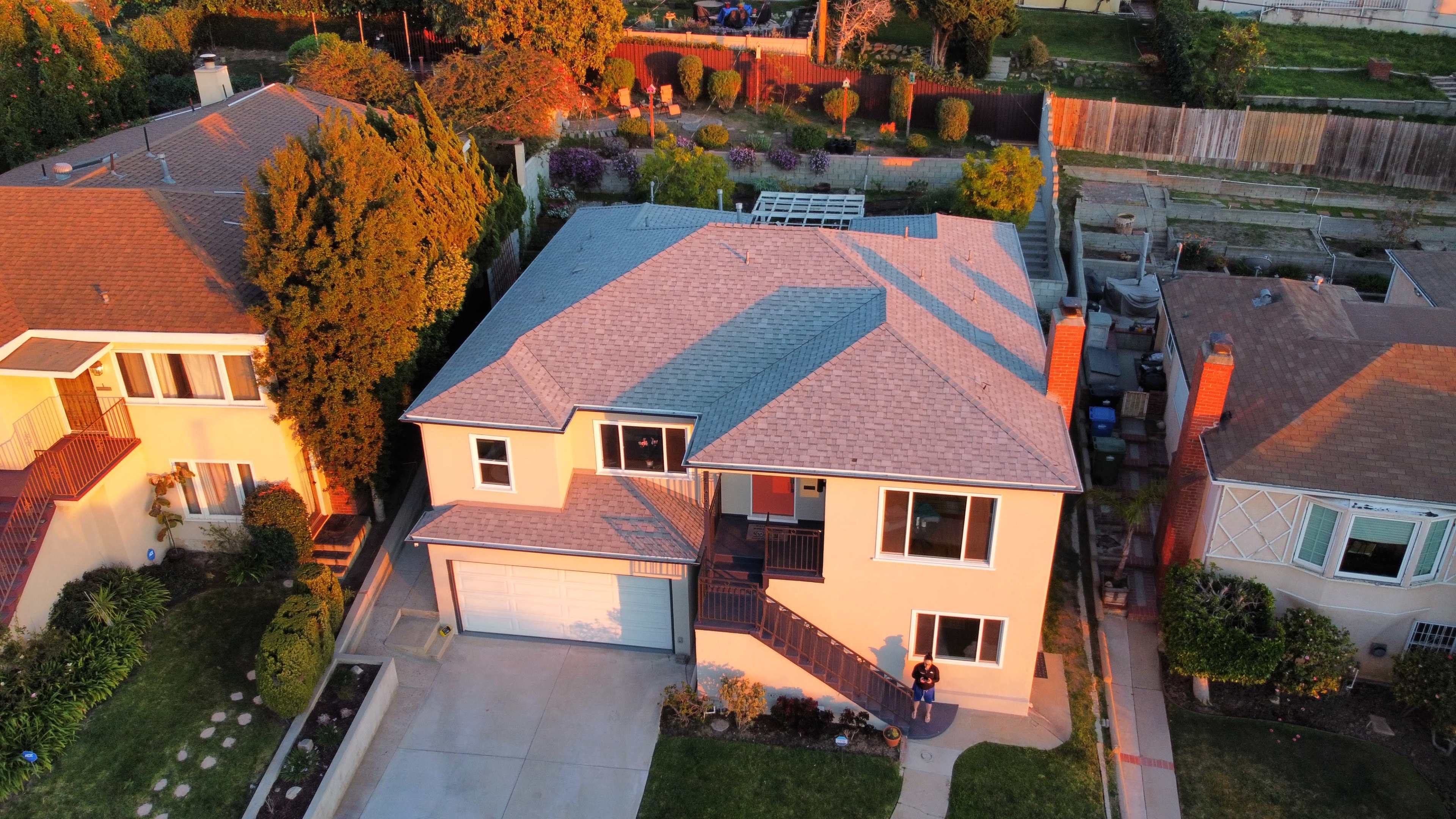 An aerial view shows a two-story house with a landscaped yard and a driveway, situated between two other homes in a suburban neighborhood.