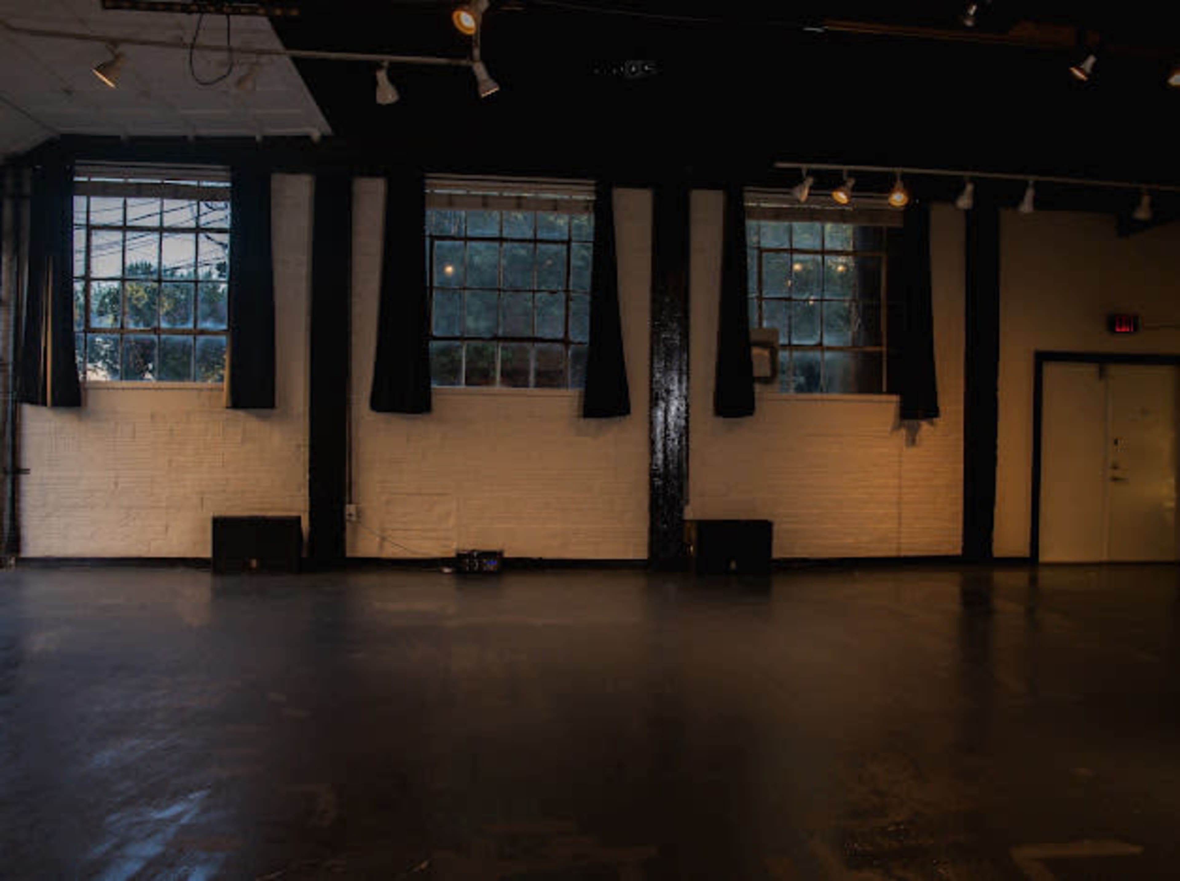 The image shows an empty indoor space with three large windows, black curtains, and a light-colored floor.